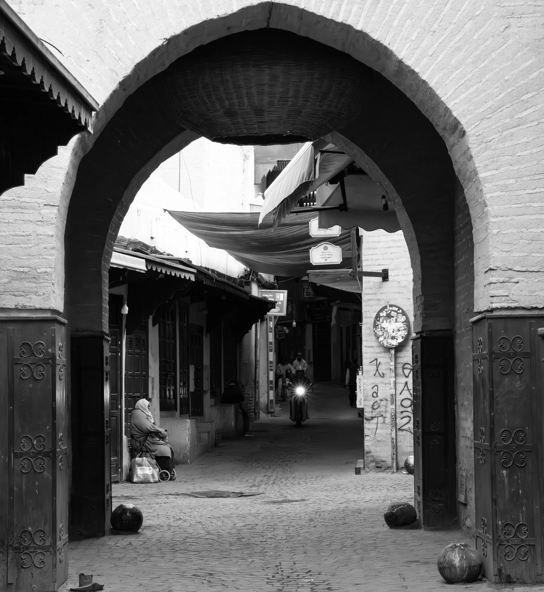 Echo Beneath the Stone, black-and-white fine art photograph by Jason Sponseller, featuring a Moroccan medina archway with historic architecture, shadow, and quiet human presence