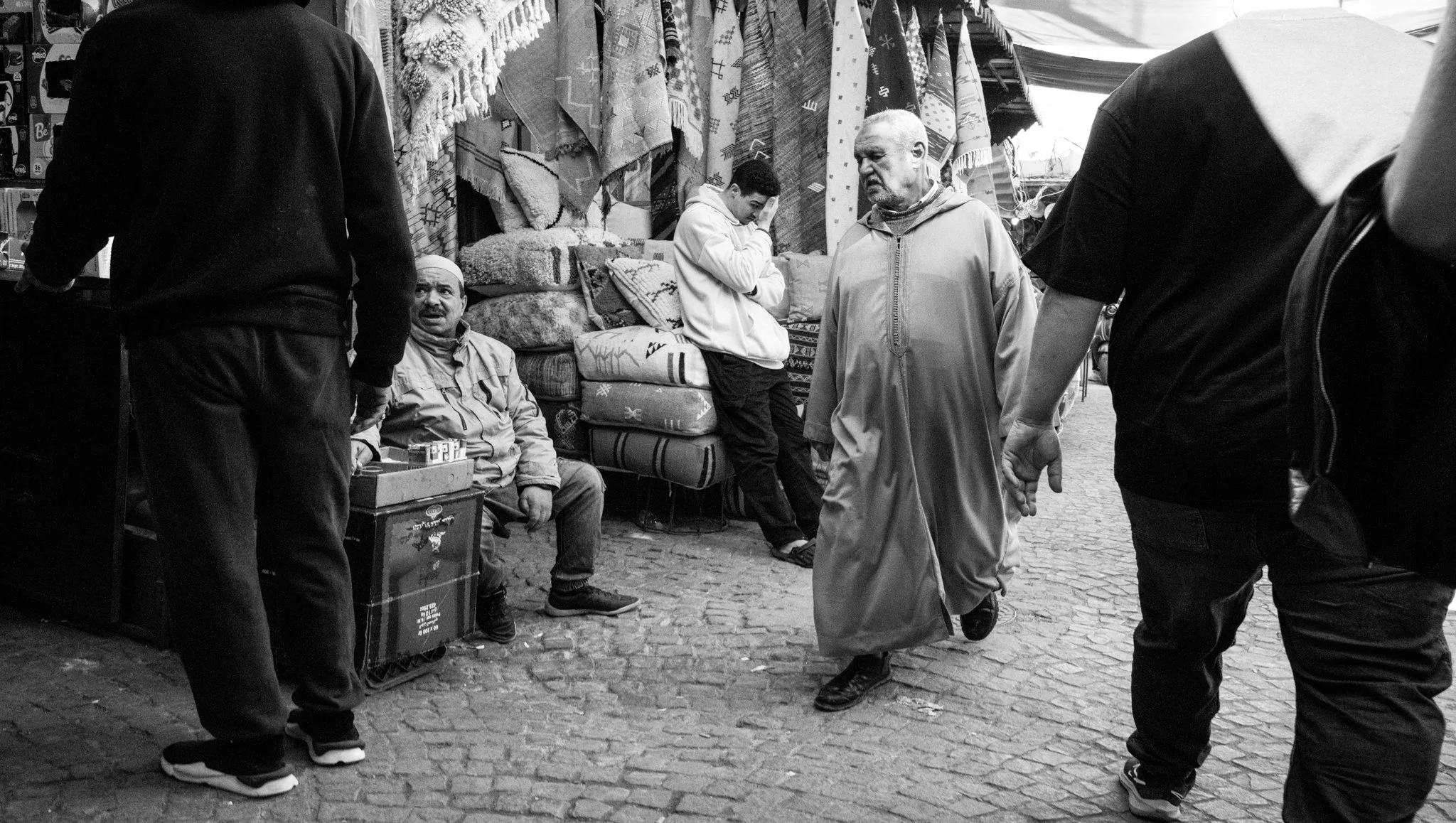 Echo Beneath the Stone, black-and-white fine art photograph by Jason Sponseller, featuring a Moroccan souk street scene with old-world architecture, market life, layered texture, and human presence