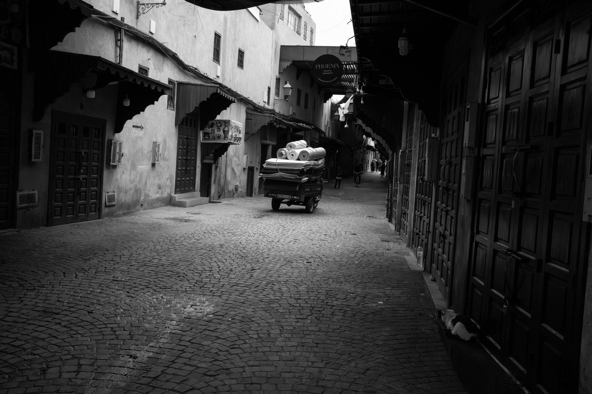 Echo Beneath the Stone, black-and-white fine art photograph by Jason Sponseller, featuring a Moroccan medina street with old-world architecture, architectural texture, shadow, and quiet human presence