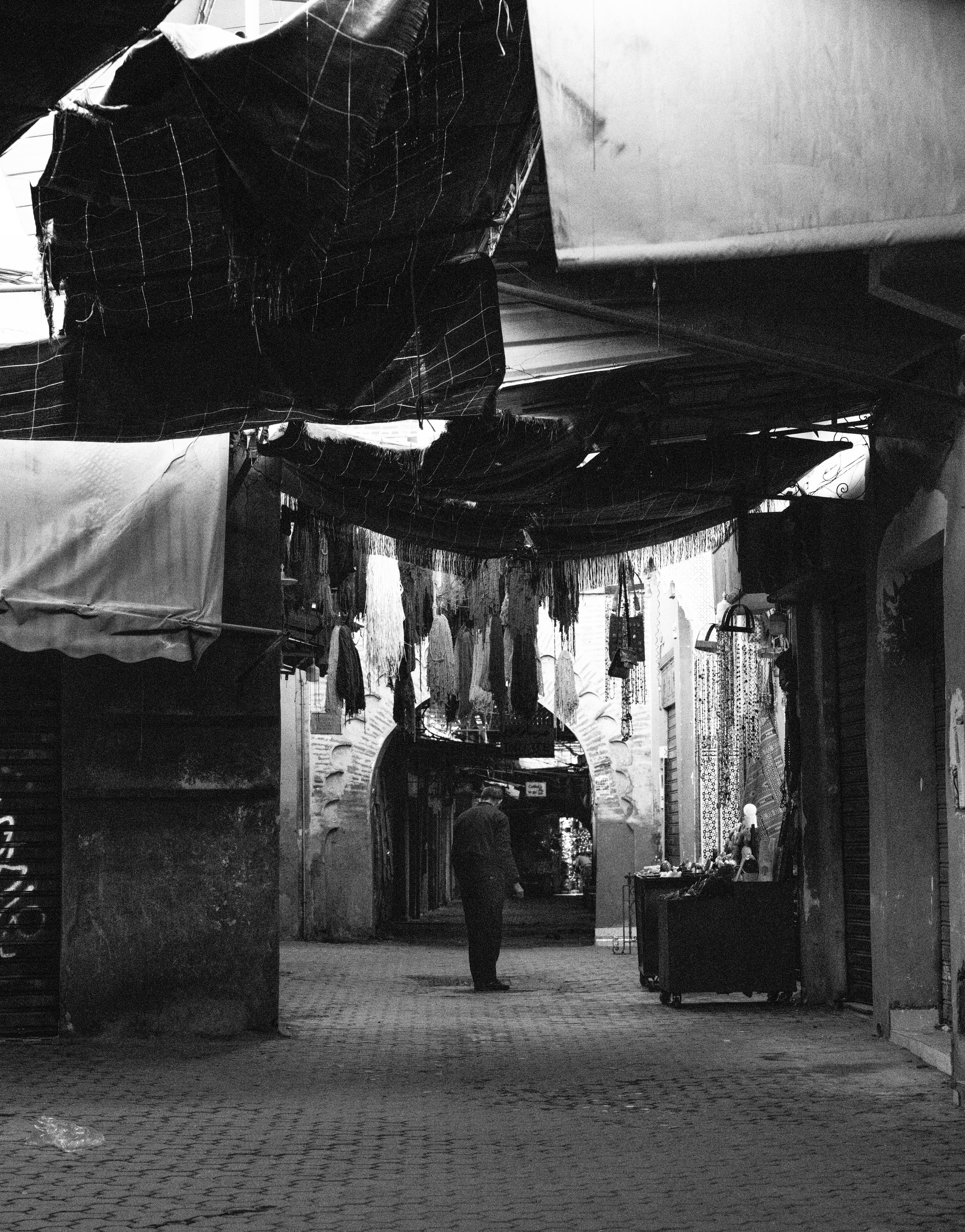 Echo Beneath the Stone, heirloom fine art photograph by Jason Sponseller, featuring a black-and-white market passage with old architecture, shadow, and human presence