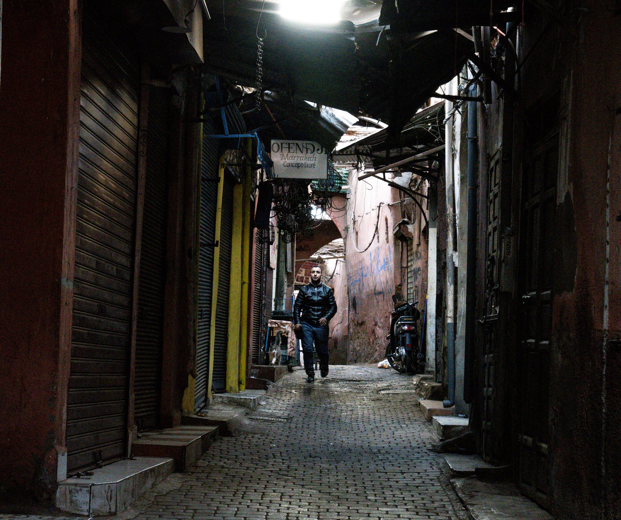 Echo Beneath the Stone, heirloom fine art photograph by Jason Sponseller, featuring a Moroccan medina alley with old-world architecture, deep shadow, color, and quiet human presence