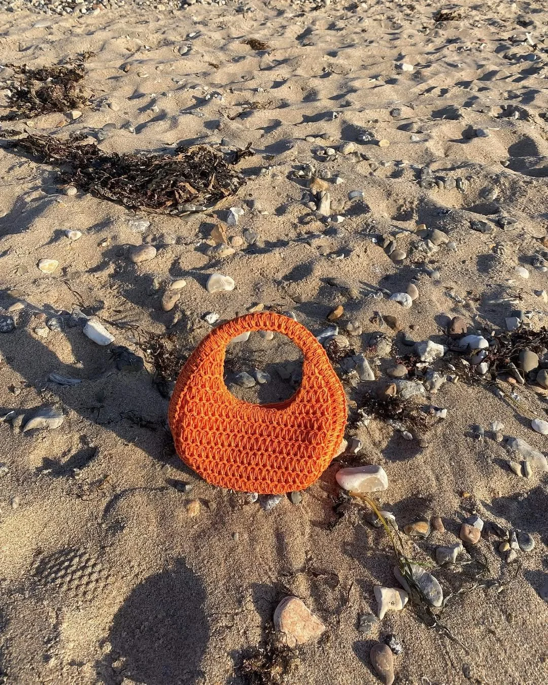 Here are the updated alt texts:
Orange crocheted handbag on beach
Handcrafted crocheted bag reflecting the artisanal craft and heritage aesthetic explored in the Cultural Signals report by Marieke Neleman, creative strategist and cultural curator.
