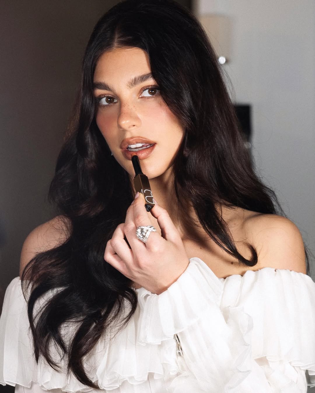 Woman with long dark hair applying lipstick from a tube.