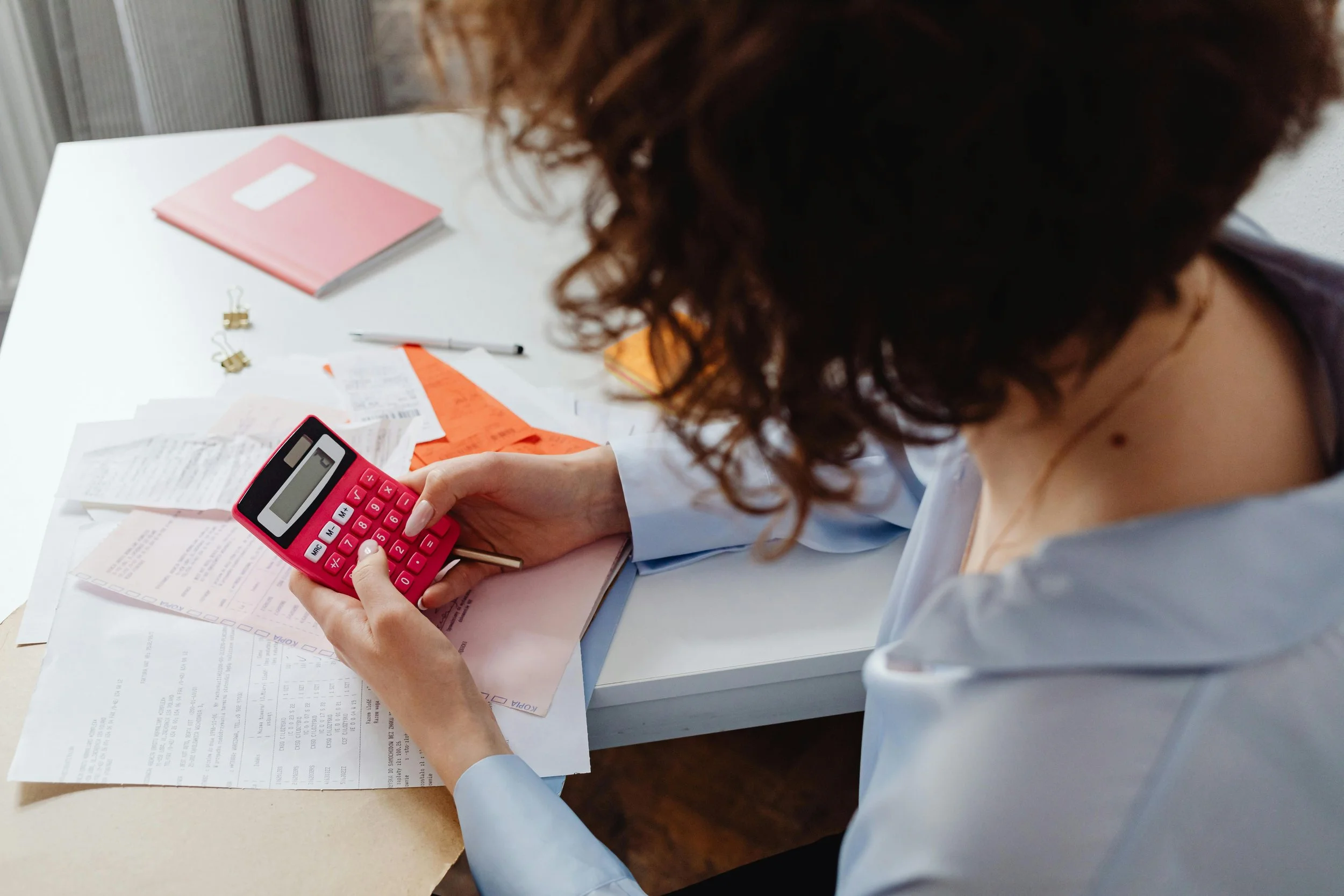 A stock photo of a women using a calculator at a desk over a pile of papers.