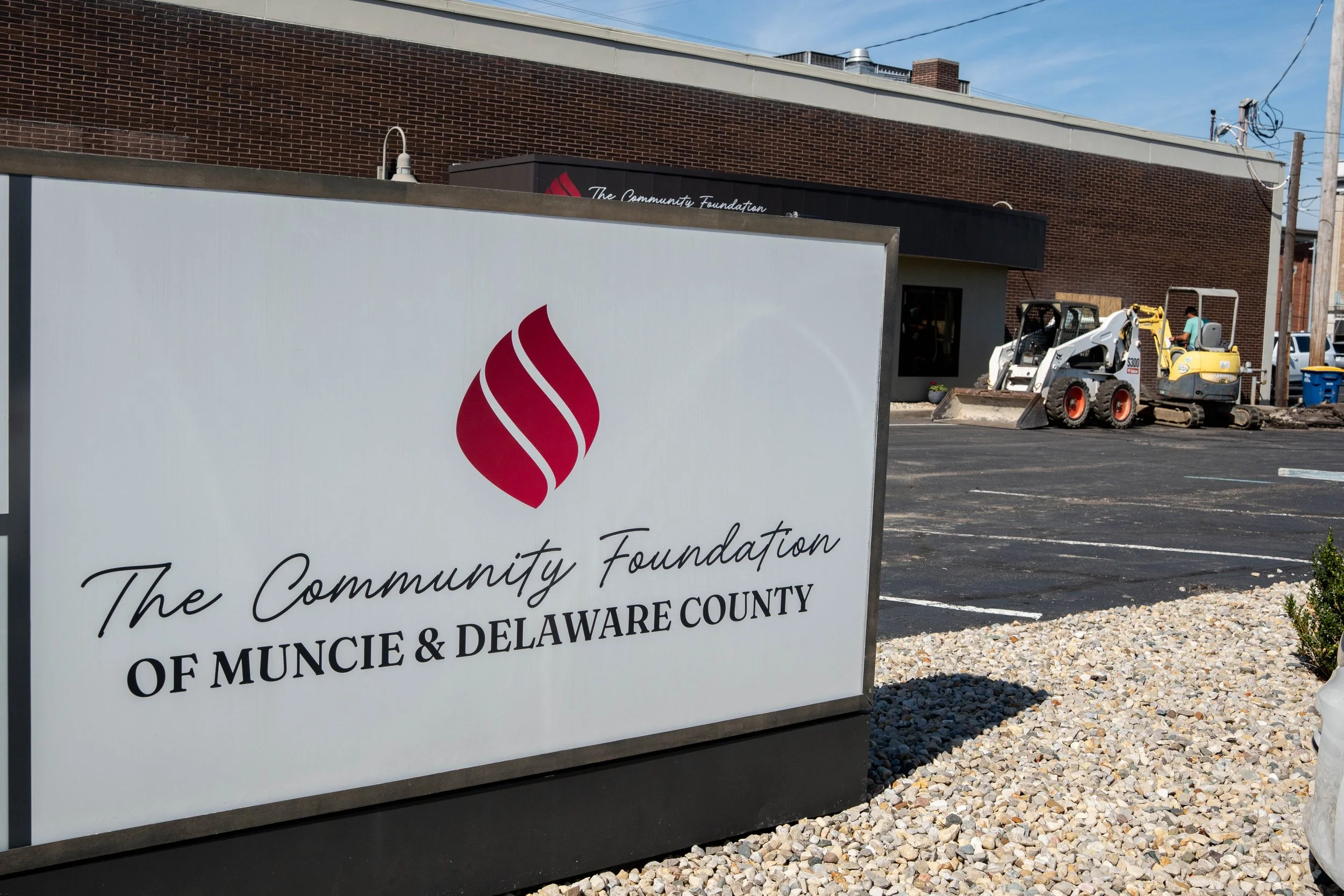 The Community Foundation logo on a white sign outside of the Foundation's brown brink building. In the background of the photo, construction equipment sits outside the building.