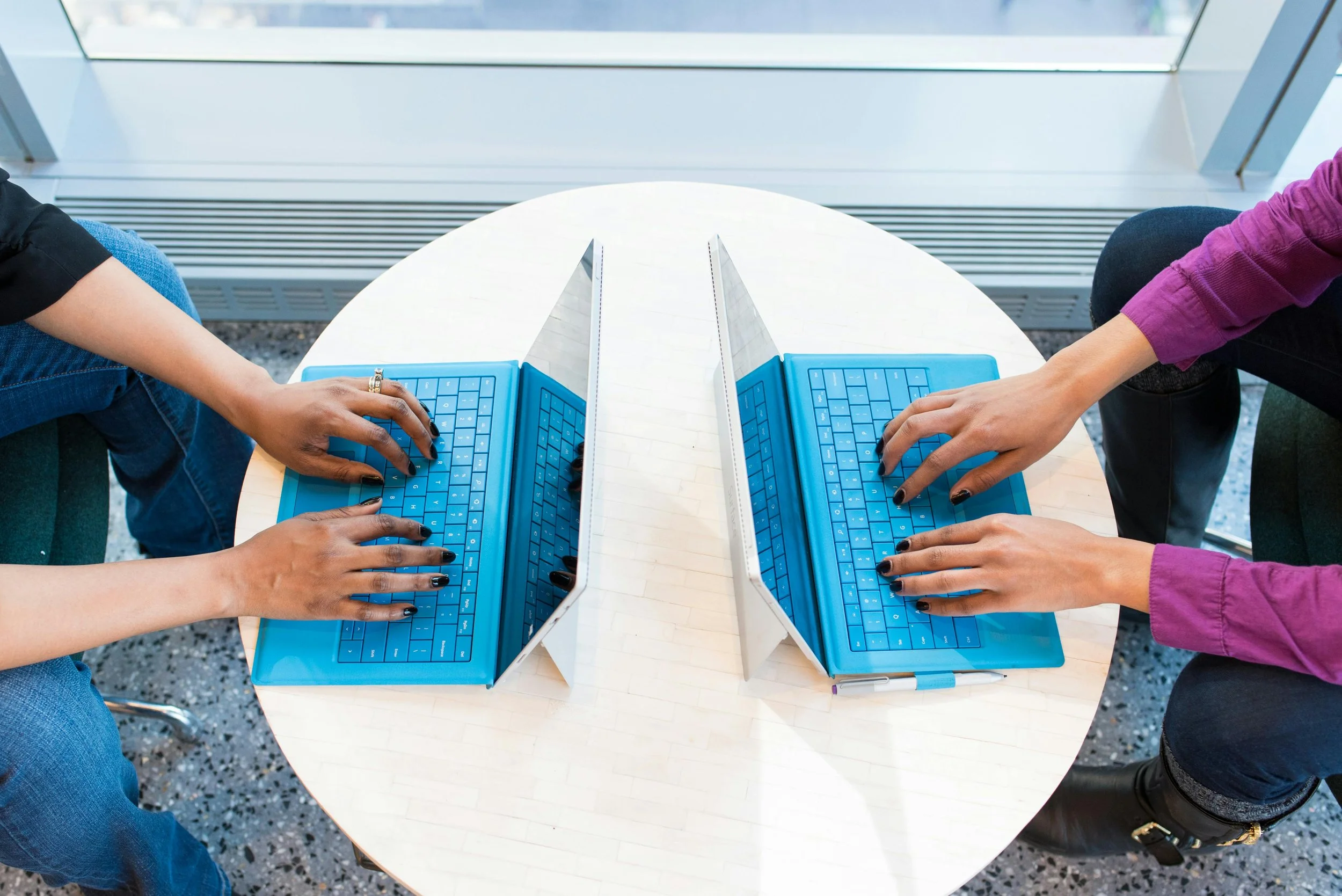Photo of two lap tops being used by two sets of hands.