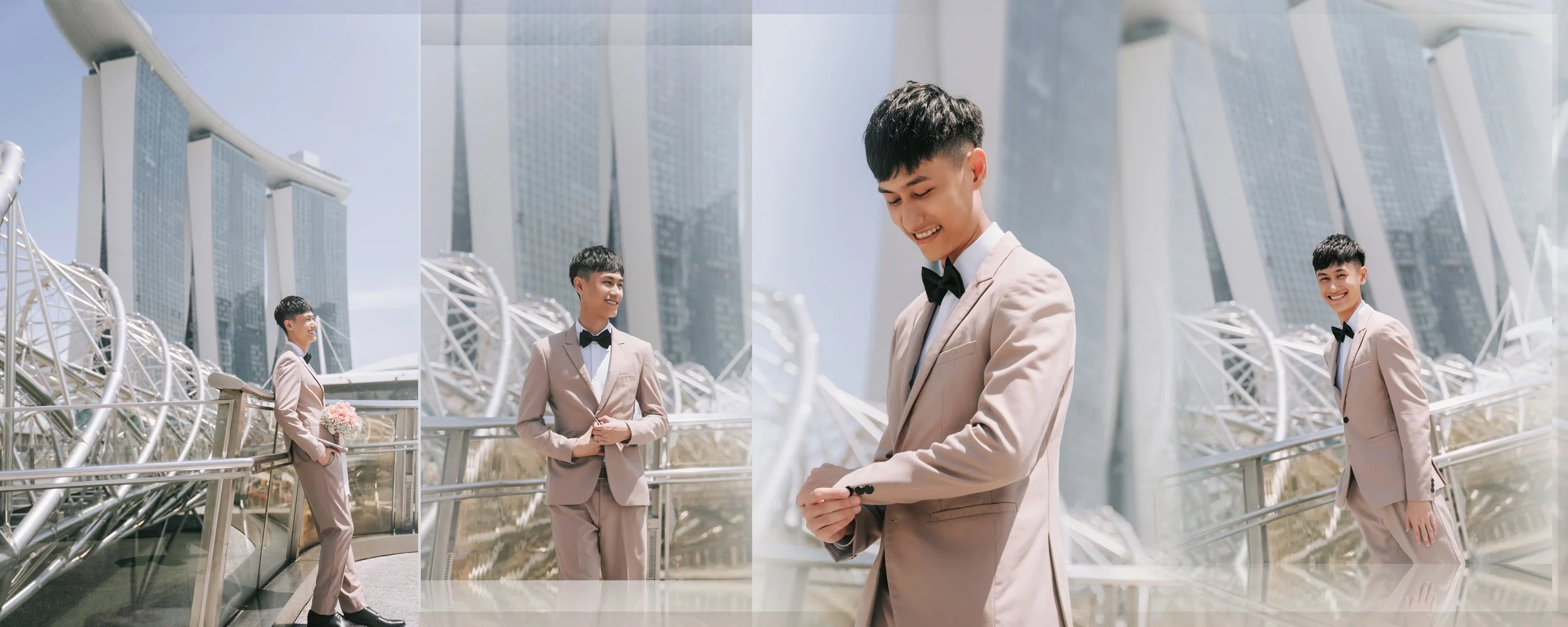 Young man in a beige tuxedo with a black bow tie standing outdoors in front of modern architectural structures and skyscrapers, holding a bouquet of pink flowers, smiling.