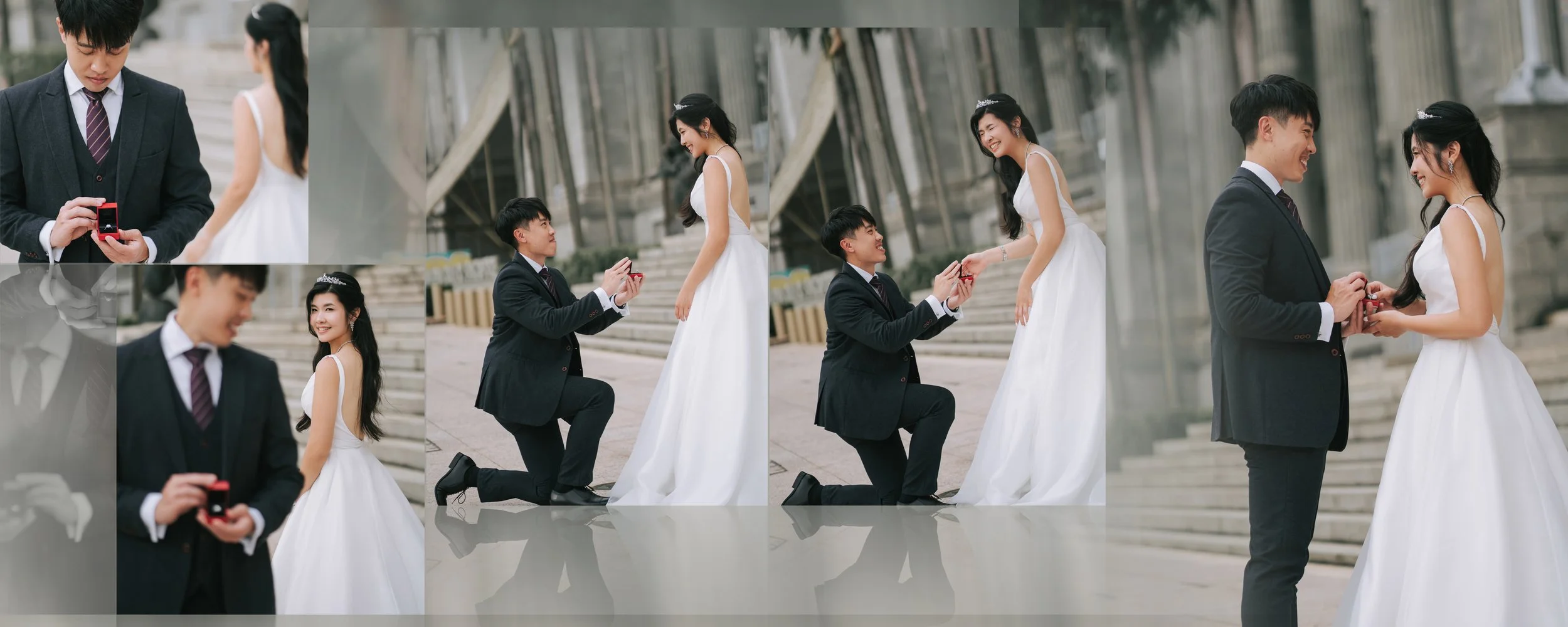 A couple during a marriage proposal photo shoot. The man is on one knee offering a ring to the woman, who is smiling and wearing a white dress and tiara. The man is dressed in a black suit and tie. The background features steps and a modern building.