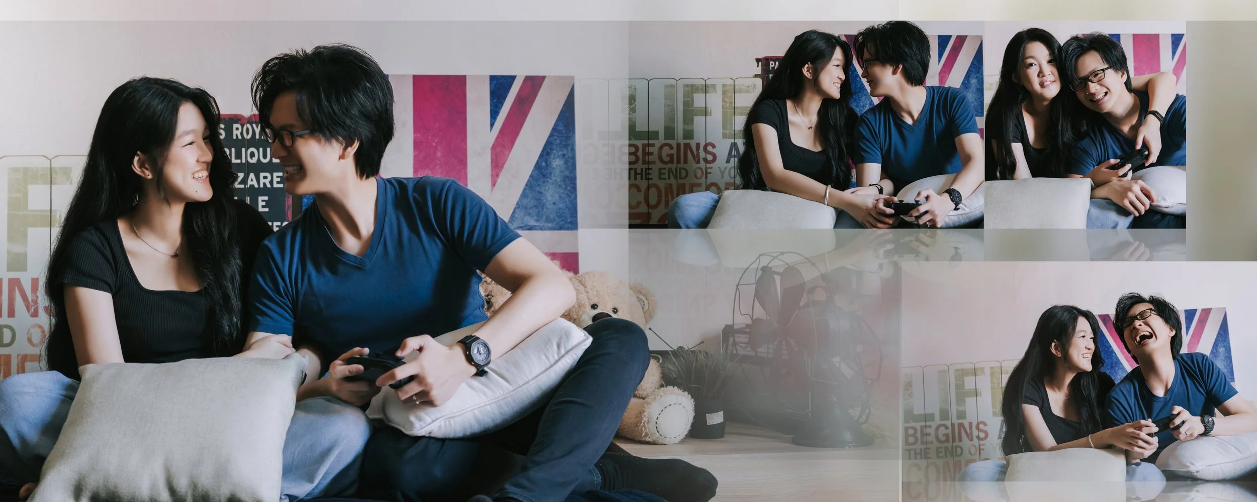 Two young Asian people, a woman with long black hair and a man with black hair and glasses, are sitting on a sofa, smiling and playing video games together in a cozy living room with colorful posters on the wall.