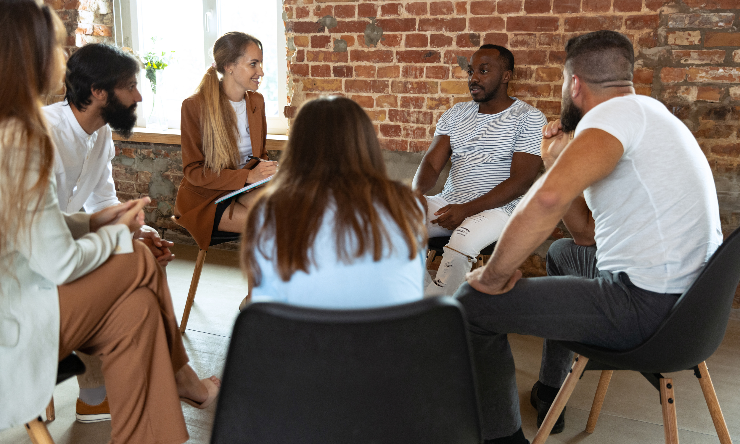 Group of six people having a discussion in a room with a brick wall.