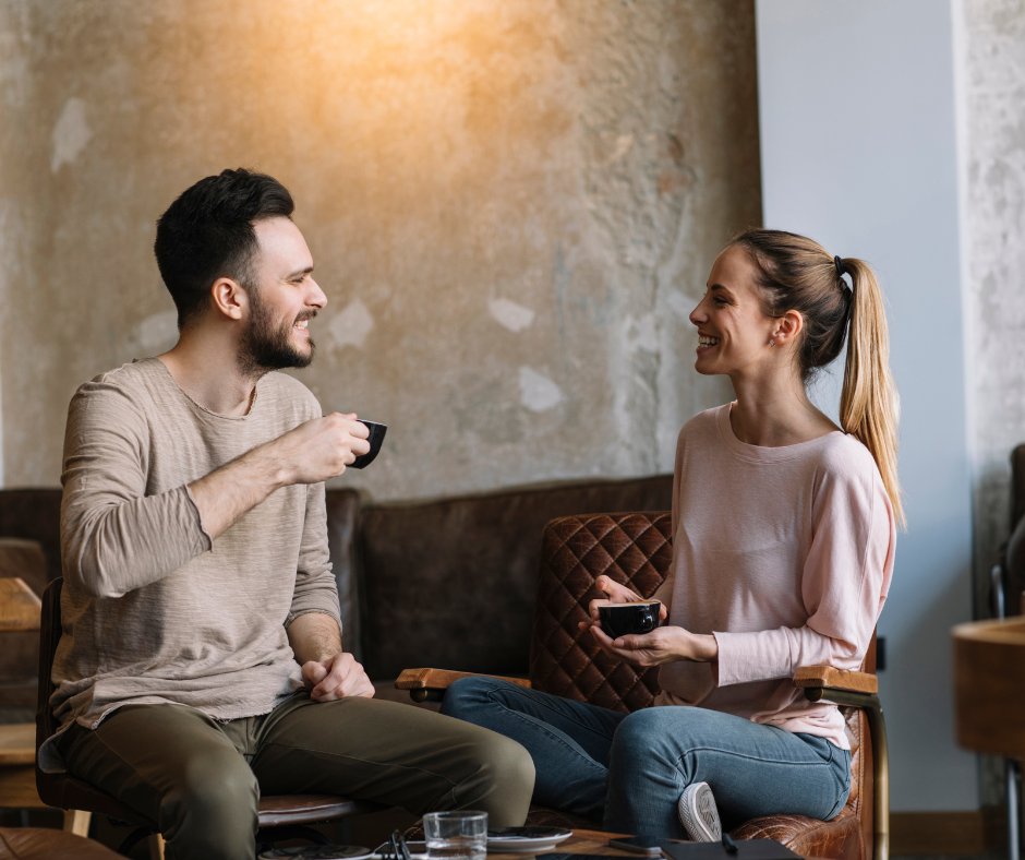 A man and woman sitting at a table in a cafe, smiling and enjoying coffee and snacks.