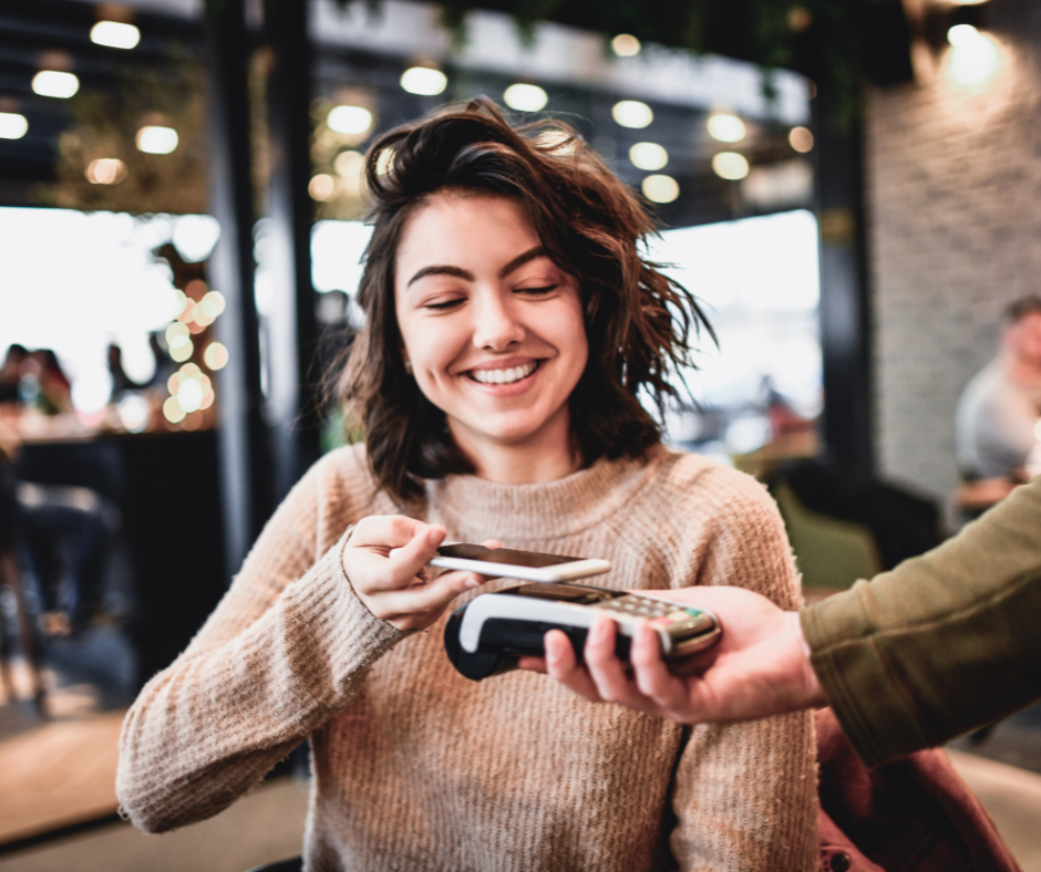 A young woman smiling as she makes a contactless payment at a cafe.