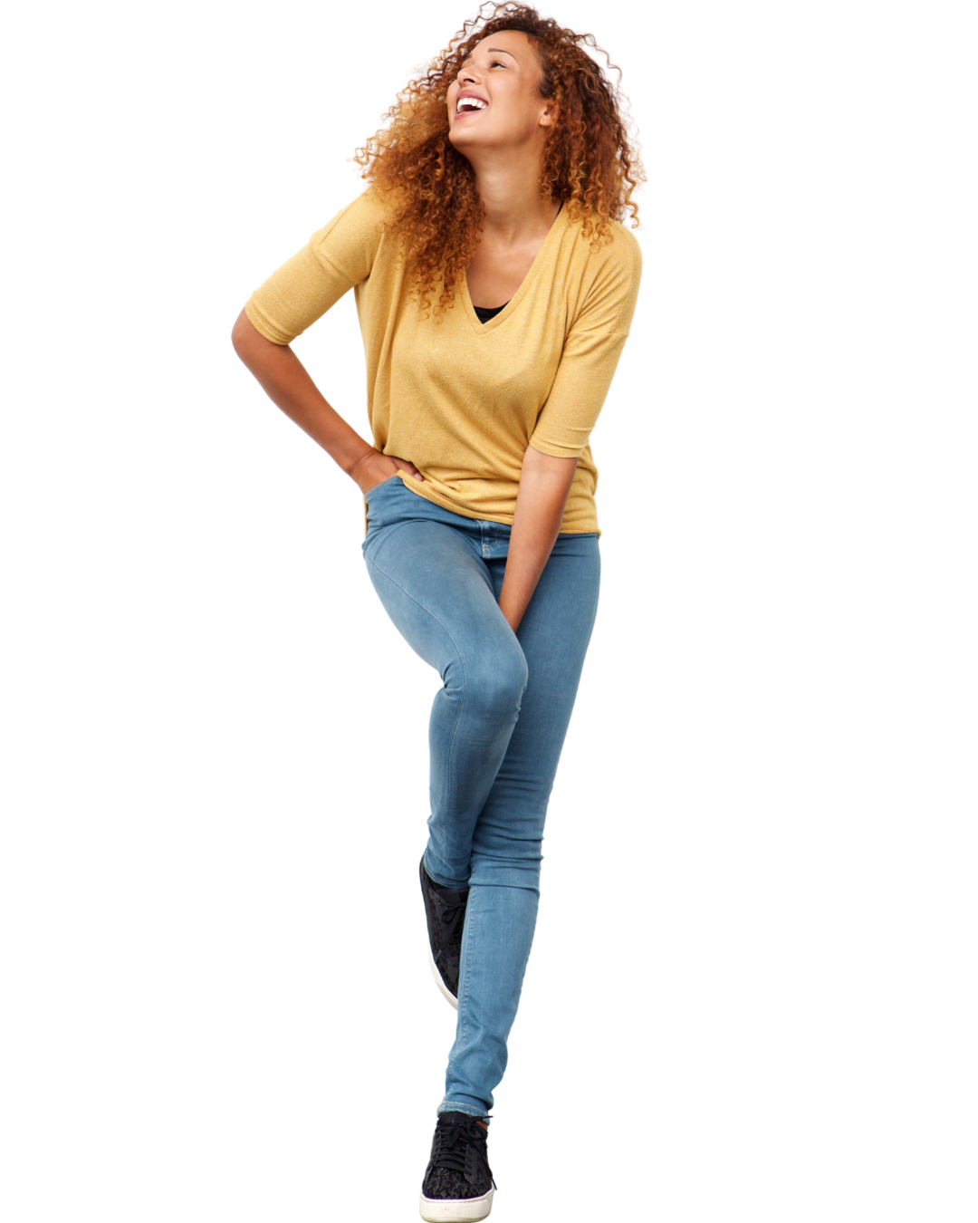 A young woman with curly hair, wearing a yellow t-shirt and blue jeans, laughing and holding her right knee with her hand, standing with one foot slightly raised.