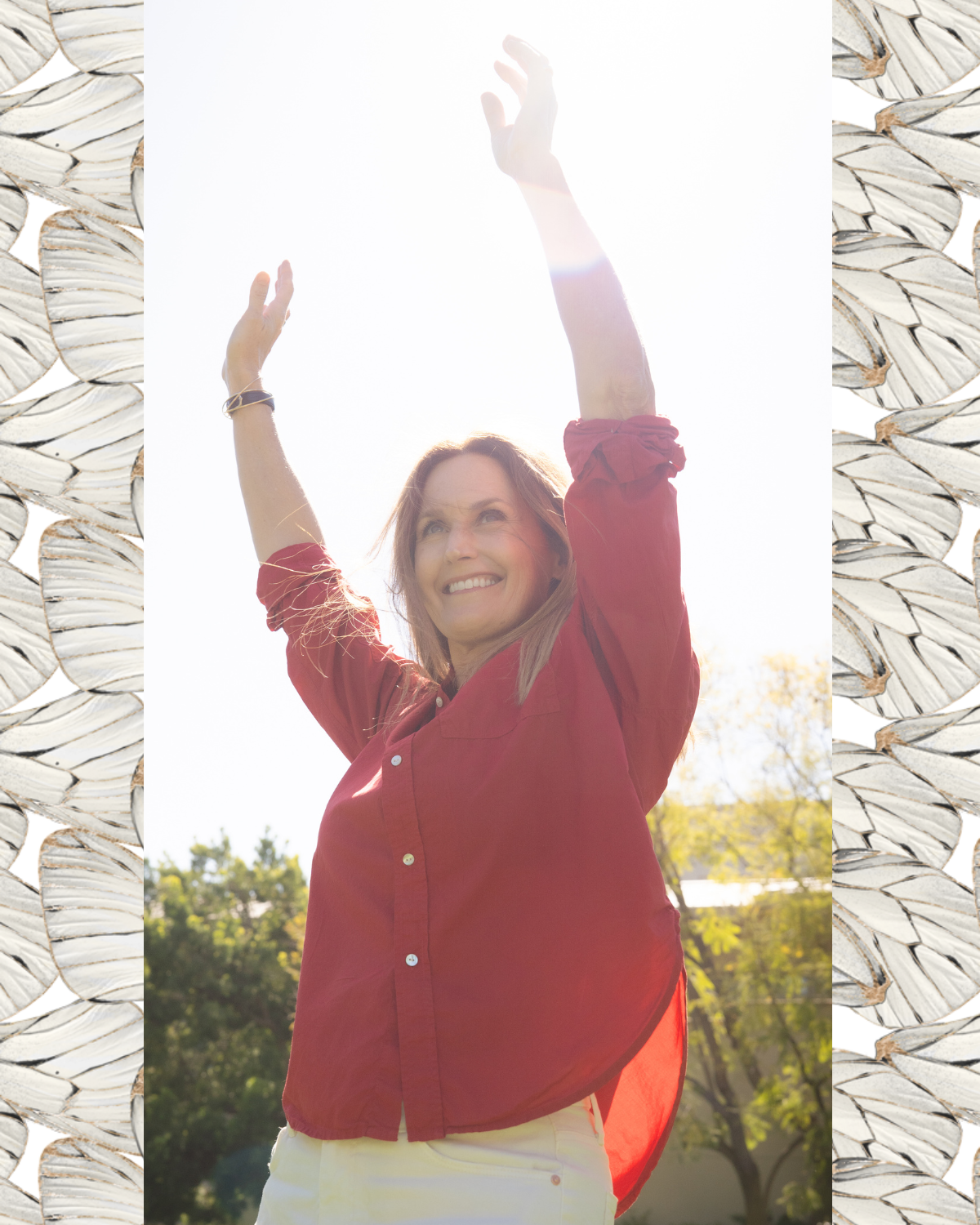 woman standing outside smiling with arms raised over her head.