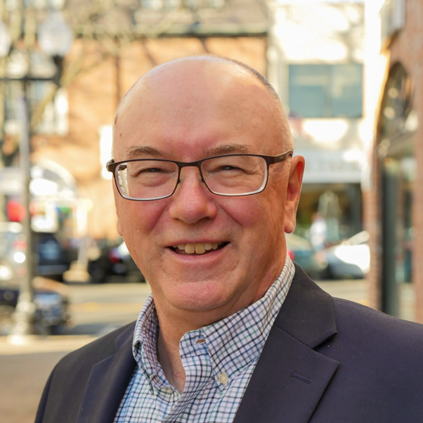 A smiling man with glasses in a business suit standing outside on a city street.