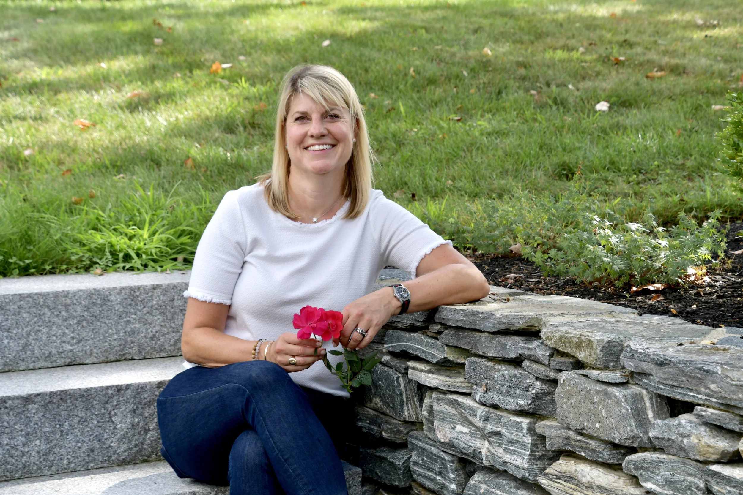 A woman in a white shirt sitting, smiling, and holding a flower