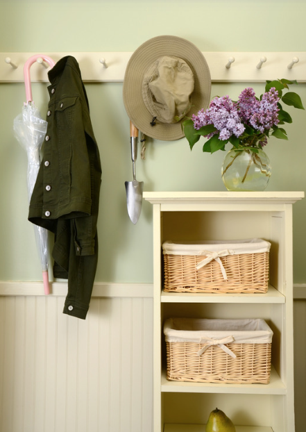 A jacket, umbrella, and hat on hooks next to cube organizers with a vase of purple flowers sitting on top.