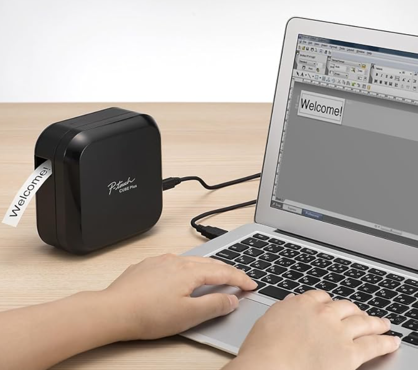 A person typing on a computer that is attached to a label maker