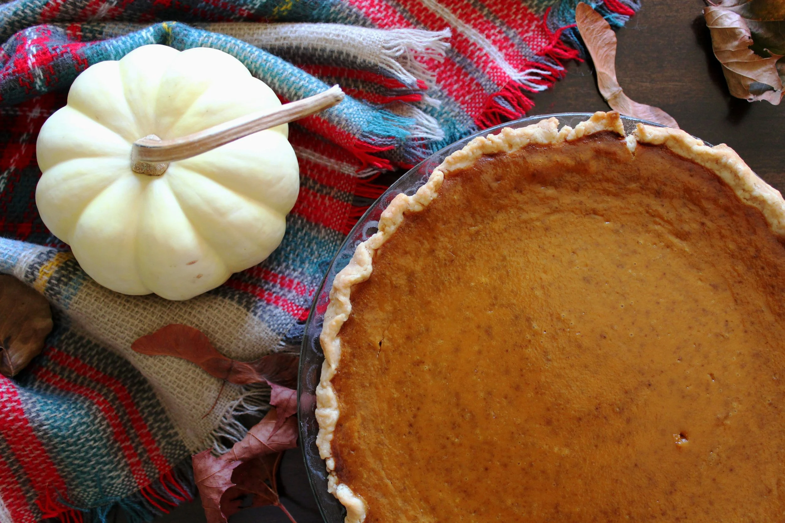 Pumpkin pie sitting next to a white pumpkin on a red, white, a blue blanket