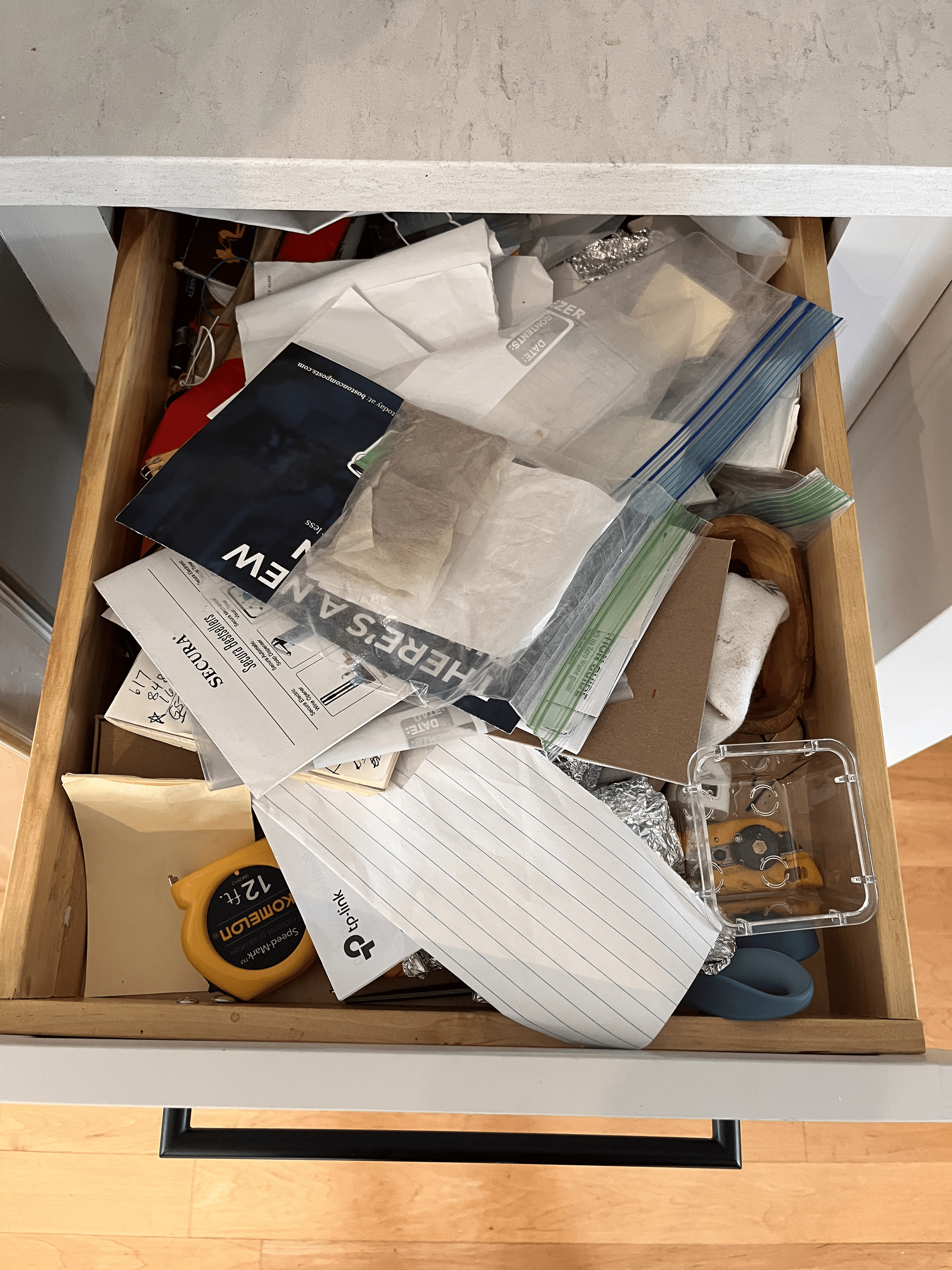 A messy drawer container plastic bags, aluminum foil, papers, scissors, and more.
