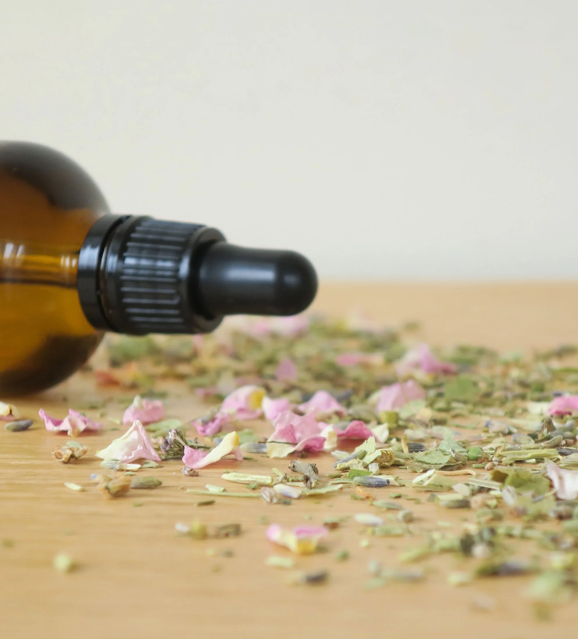 Glass dropper bottle lying on a wooden surface surrounded by dried herbs, lavender, rose and linden.