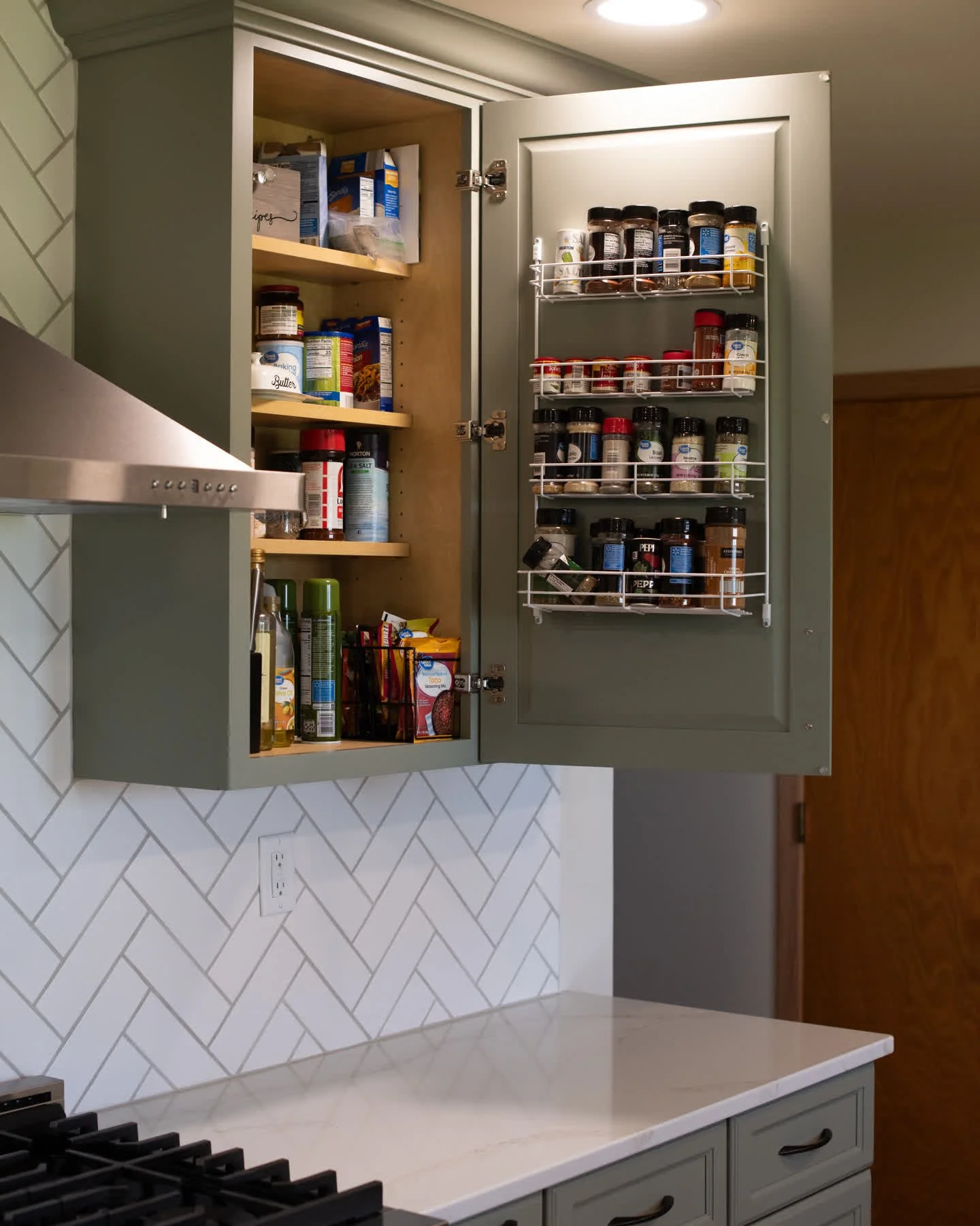 From dated to dreamy &mdash; and now incredibly organized! ✨
This remodel features sage green cabinets, warm wood floors, and a crisp herringbone backsplash, but the real magic is behind the doors: a hidden microwave cabinet, pull-out spice storage, 