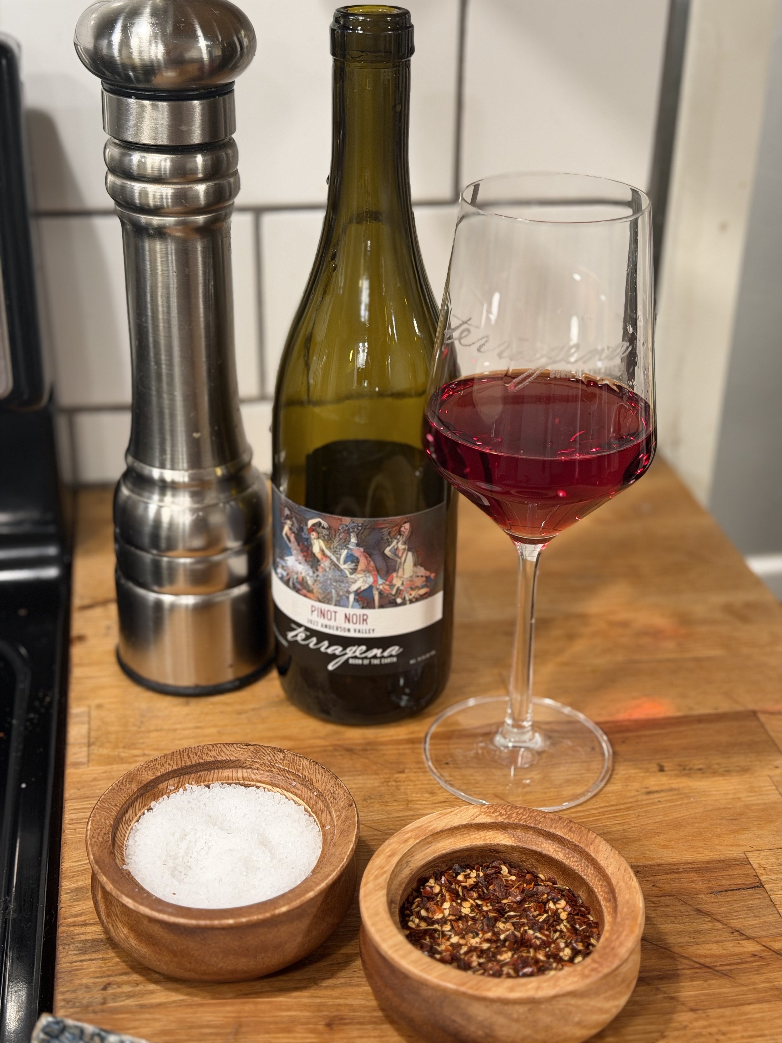 Close up photo of Terragena Anderson Valley Pinot Noir with sea salt and chili pepper flakes plus black pepper grinder for the recipes and wine pairing section