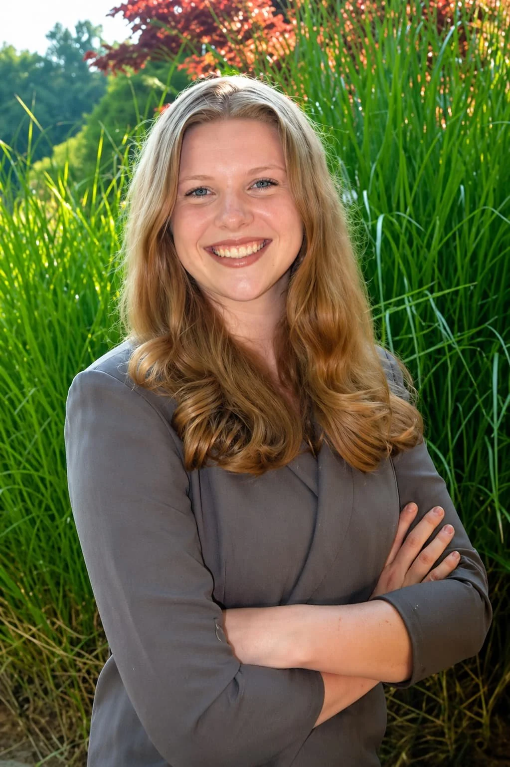 Portrait of Haleigh Champagne, Outreach Coordinator at Hearth Counseling & Consulting, smiling with arms crossed, wearing a magenta top, standing in front of a brick wall.