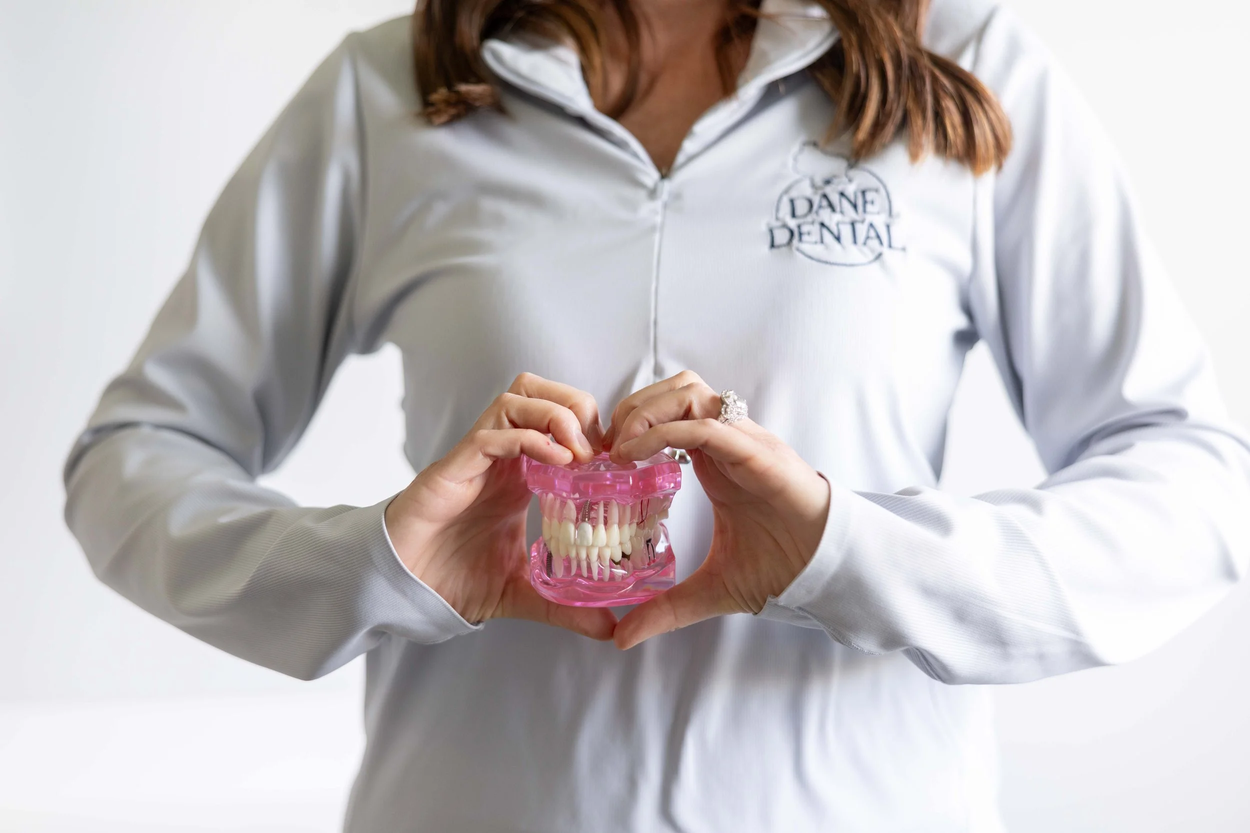 Person wearing a white jacket with a 'Dane Dental' logo holding a pink dental model with teeth.