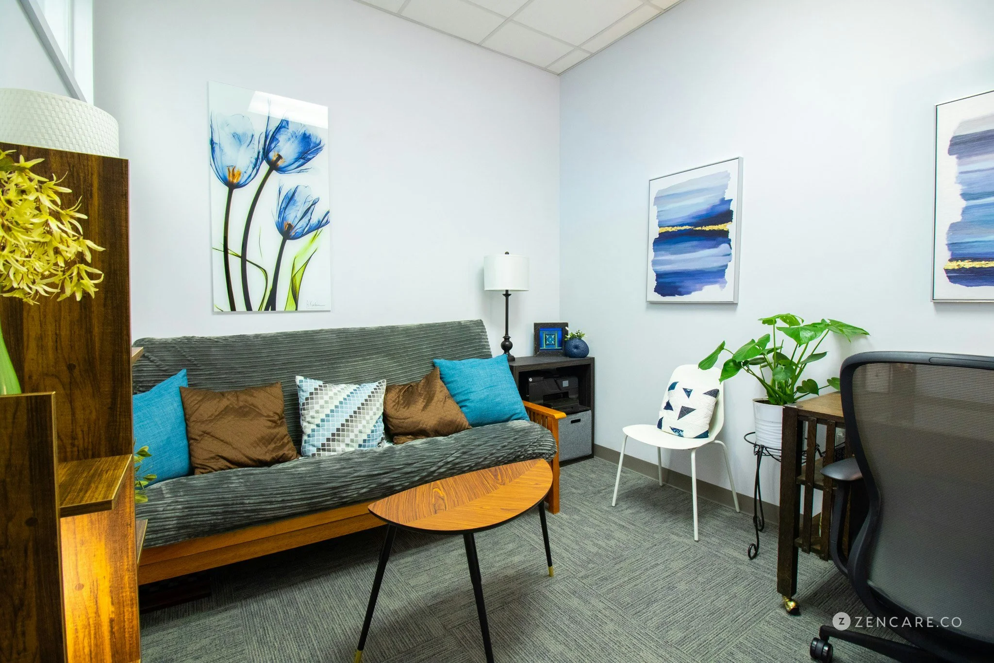 Comfortable and private therapy office in Rhode Island set up for anxiety counseling sessions with couch that has pillows, abstract blue and white paintings.
