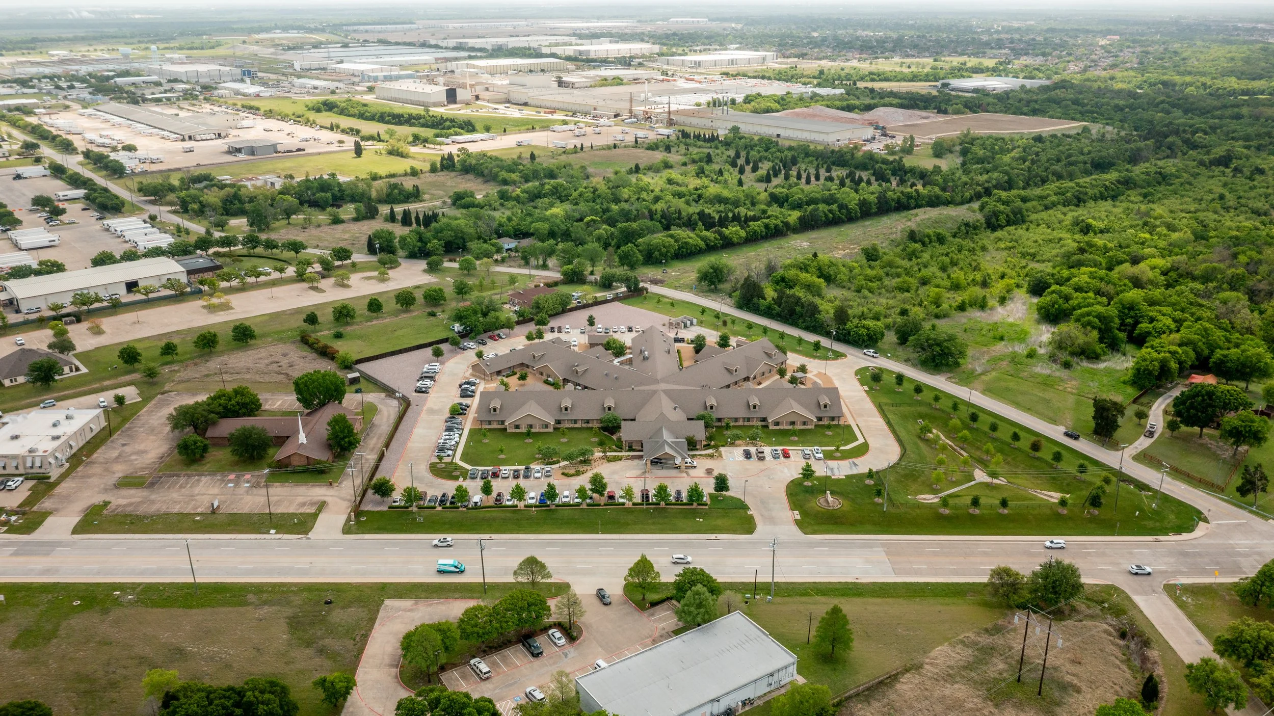 An aerial view of a commercial and residential area with green trees, parking lots, and roads.