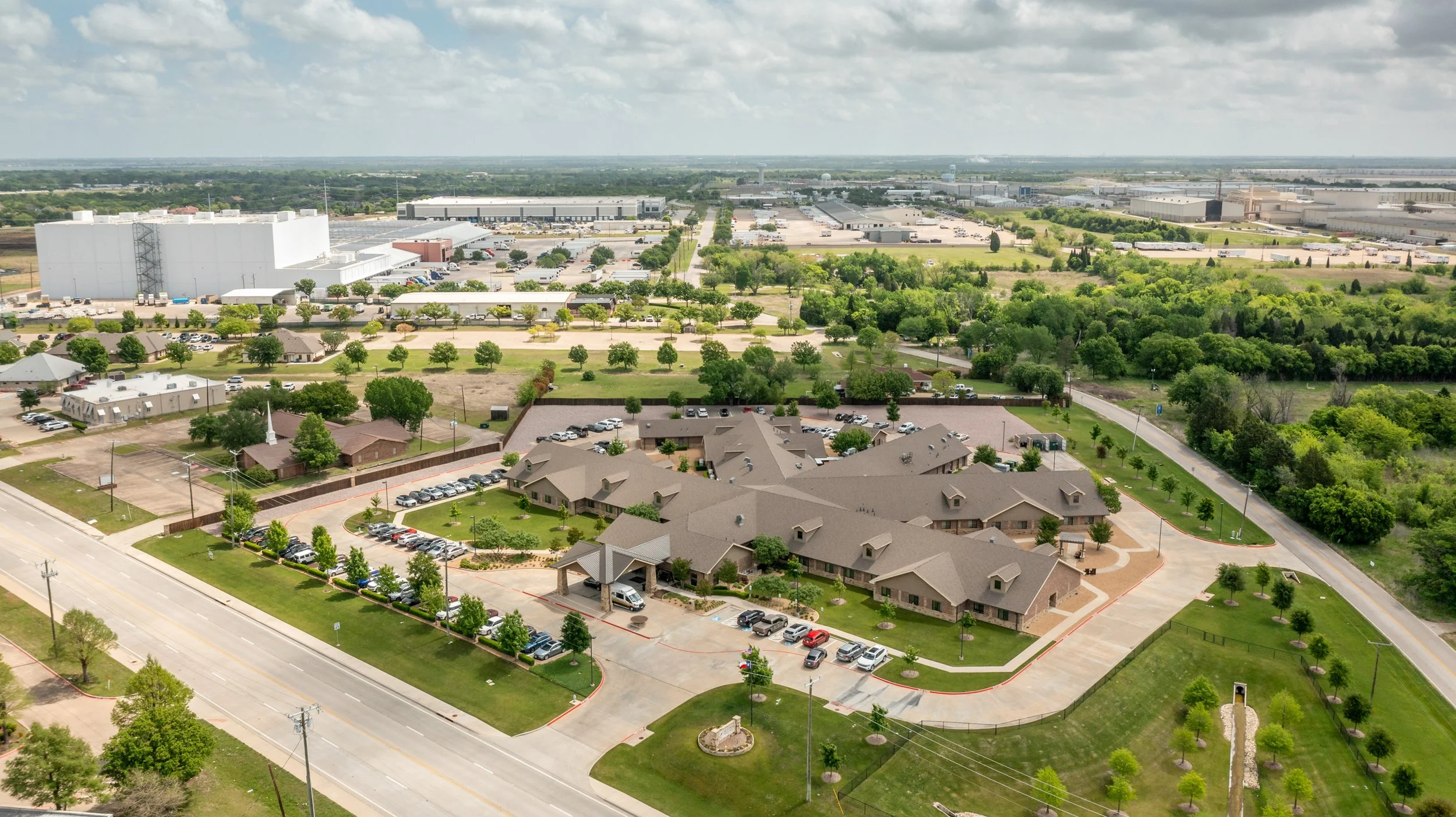 Aerial view of a suburban neighborhood with a large industrial complex and green trees.