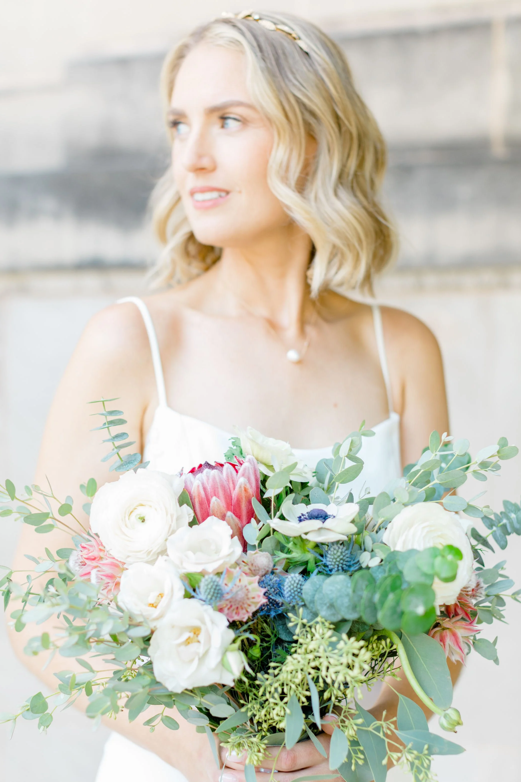 A woman in a white dress holding a vibrant bouquet of flowers, with a soft focus background.