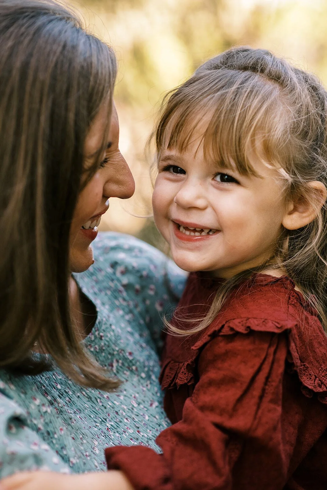 Close-up of a mother and daughter smiling face-to-face during an outdoor lifestyle photoshoot