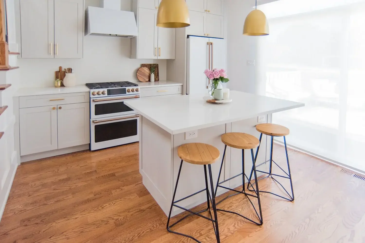 Kitchen island with wood-and-metal counter stools, with the Café matte white range and refrigerator behind it