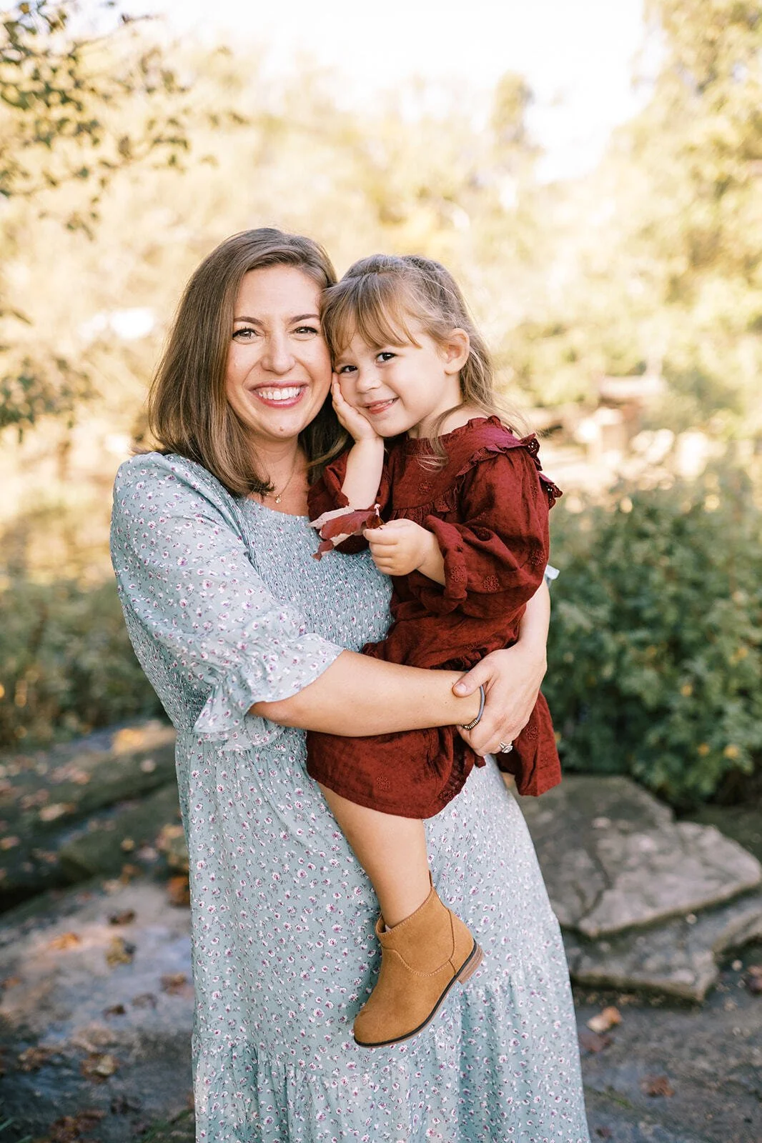 Mother holding her daughter and smiling at the camera during a natural outdoor mother-daughter photo session