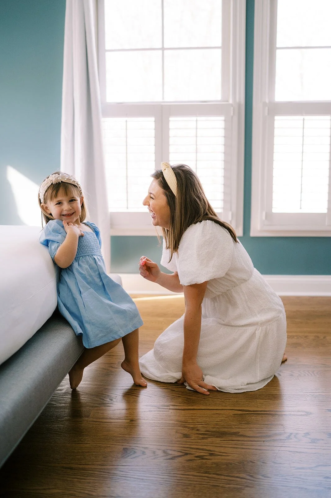 Mother kneeling and laughing with her young daughter during a candid indoor mother-daughter photoshoot