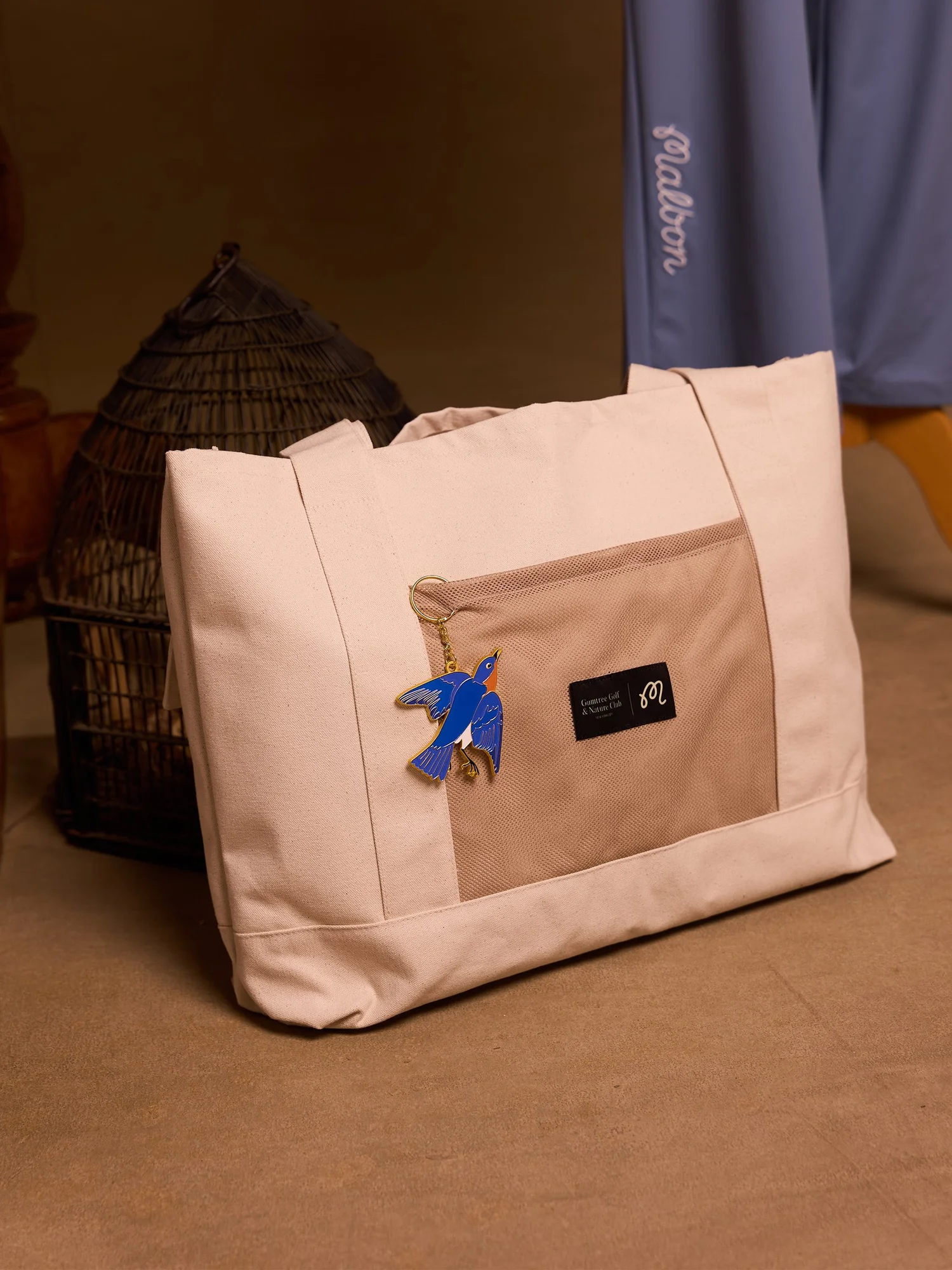 Malbon x GGNC Birds of Georgia utility tote with a bluebird keychain beside a birdcage