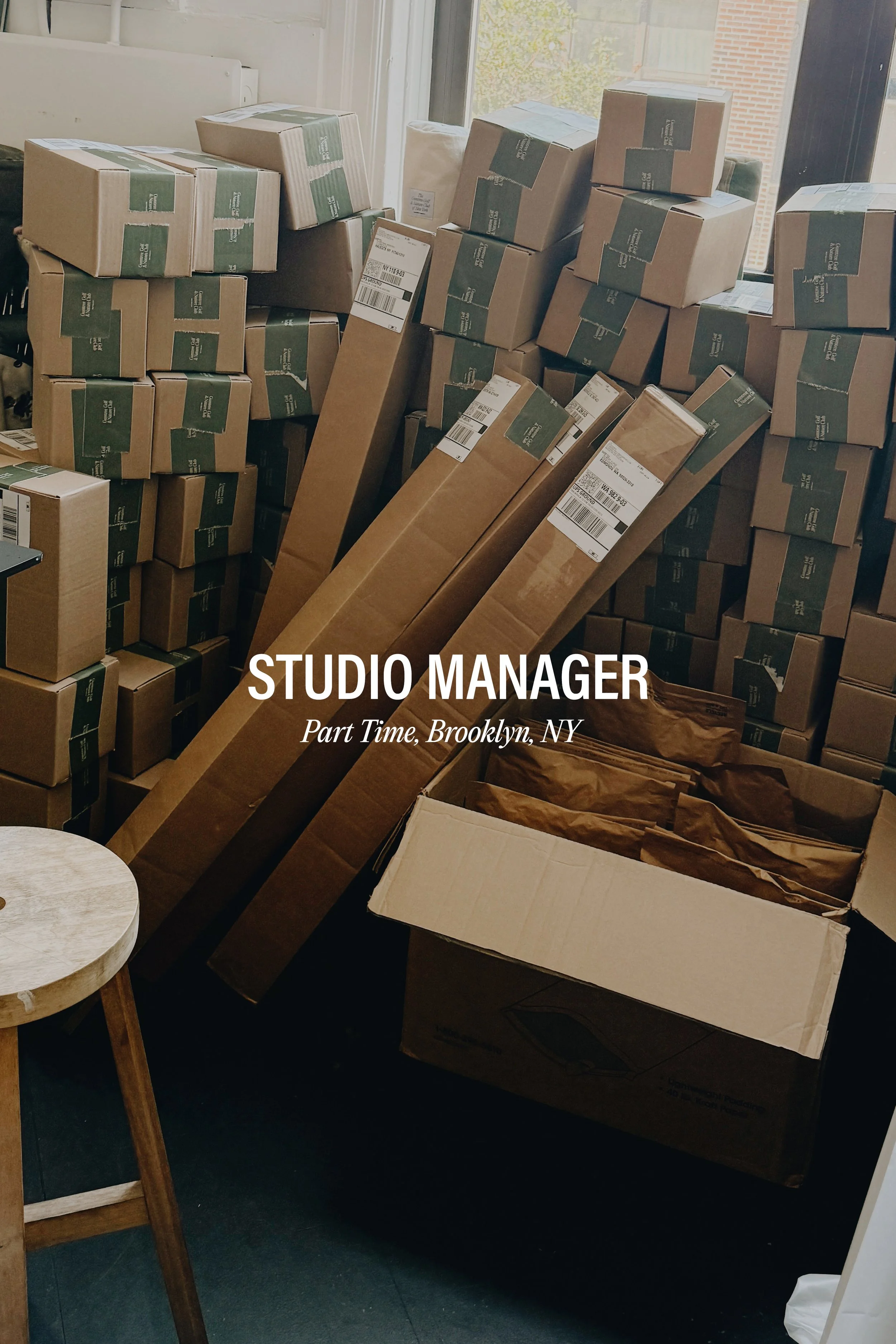 A room filled with stacked cardboard boxes, some labeled with shipping labels, and brown paper packaging, indicating a storage or packing area.