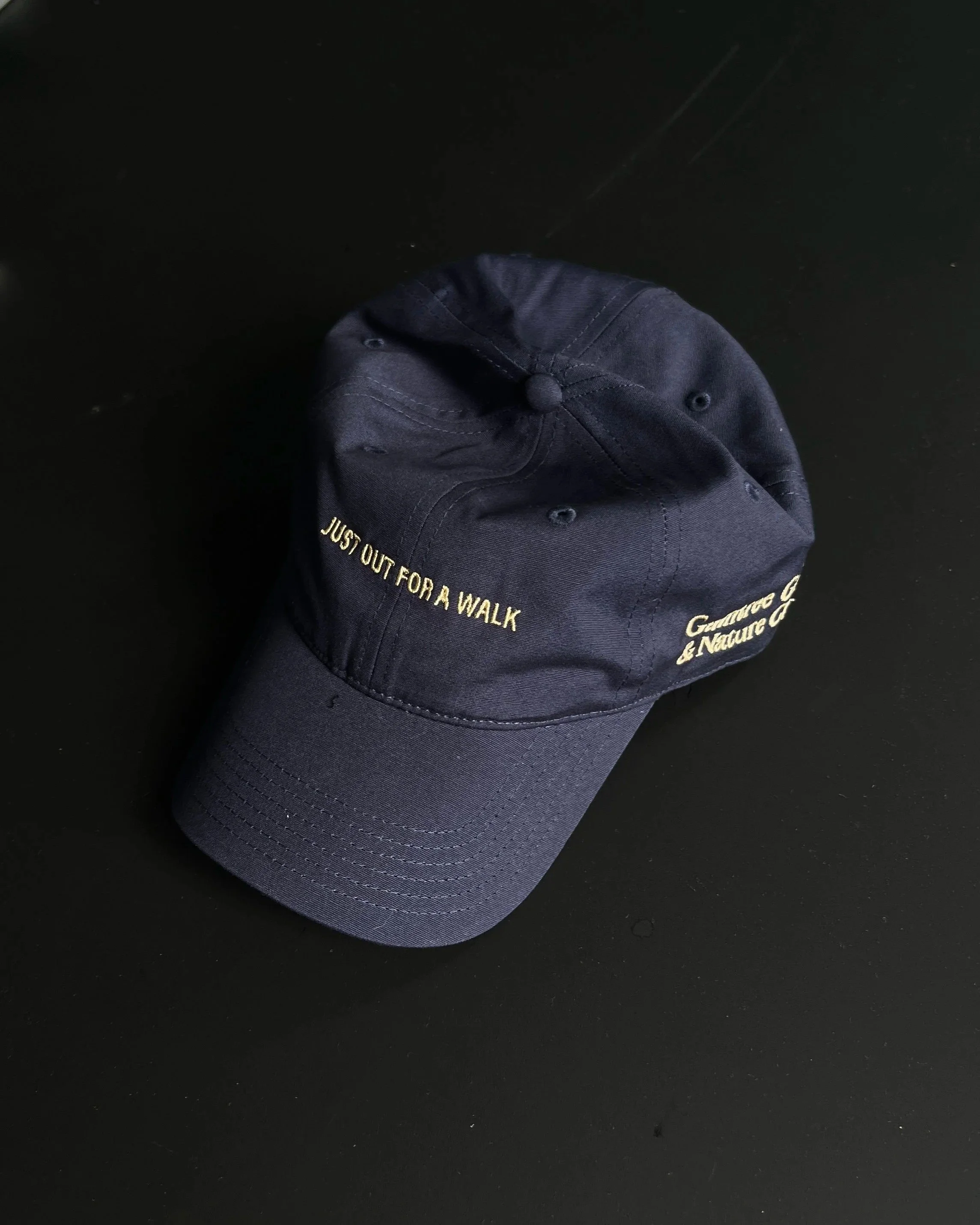Navy and gold Just Out For A Walk dad hat on a black background