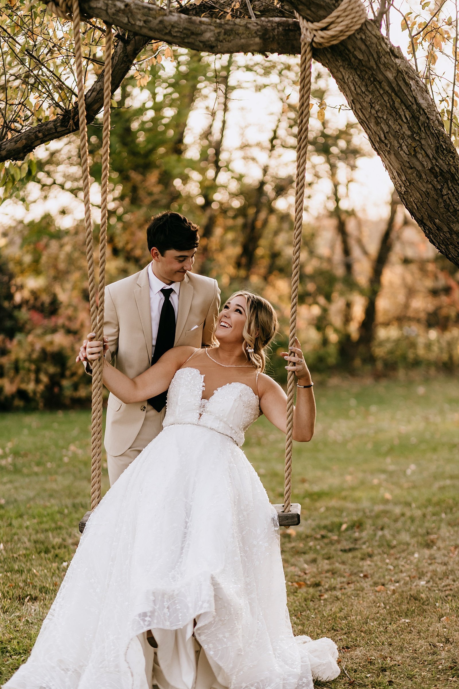  Bride swinging on a tree swing with groom pushing her for their Minnesota fall wedding 