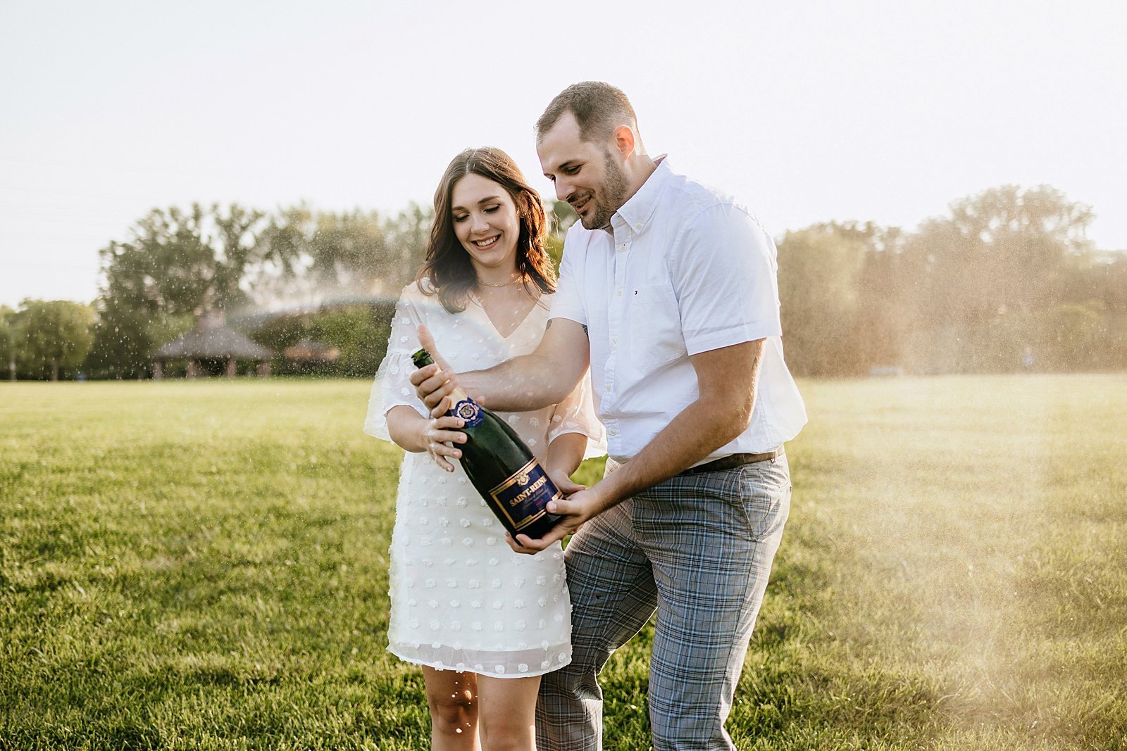  Couple popping champagne during their sunrise engagement session in a field.  