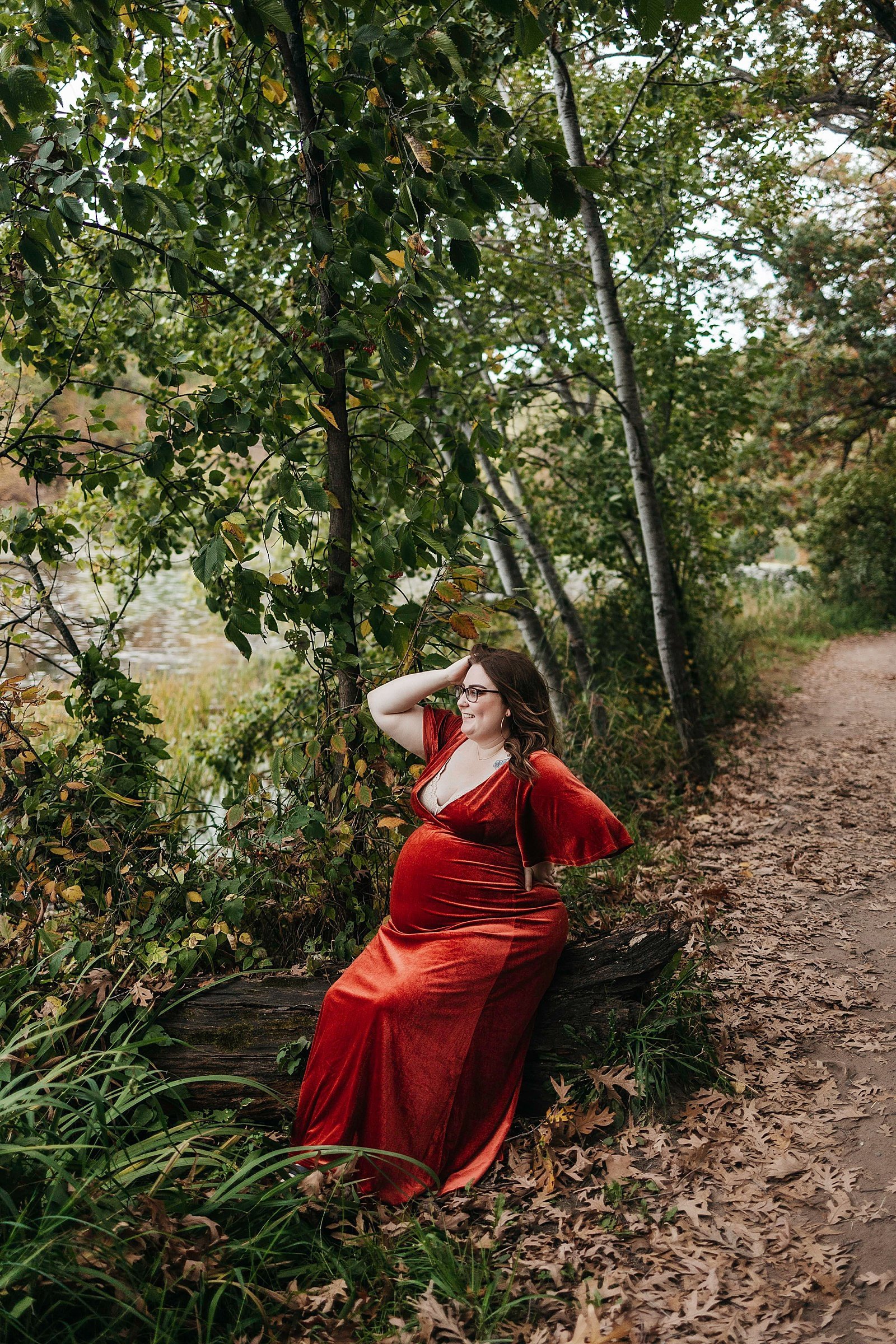  Woman in red velvet dress in the woods for her maternity session with Minneapolis photographer, McKenzie Berquam. 