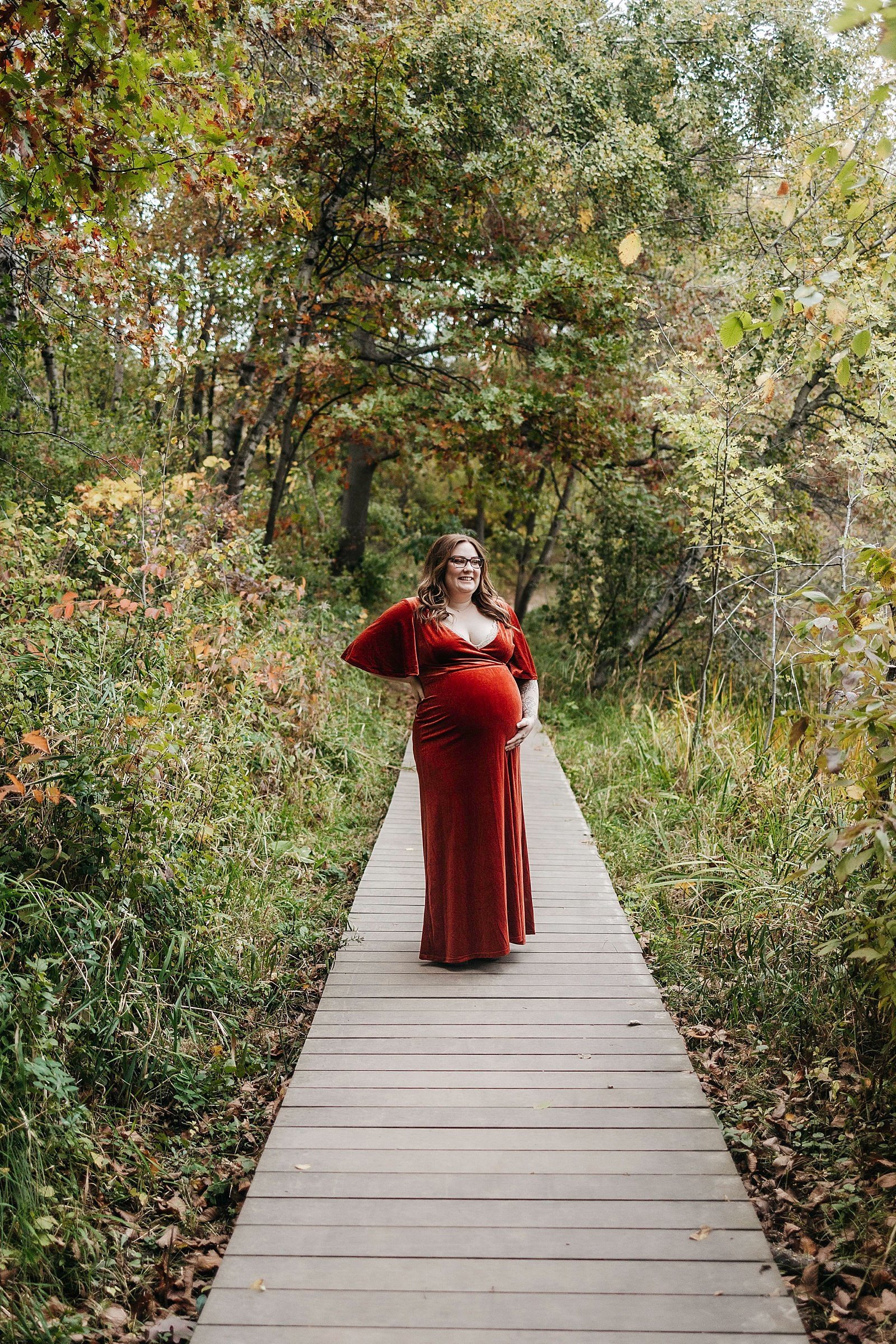  Woman in red dress and pregnant belly in the woods for a photo shoot with photographer McKenzie Berquam. 
