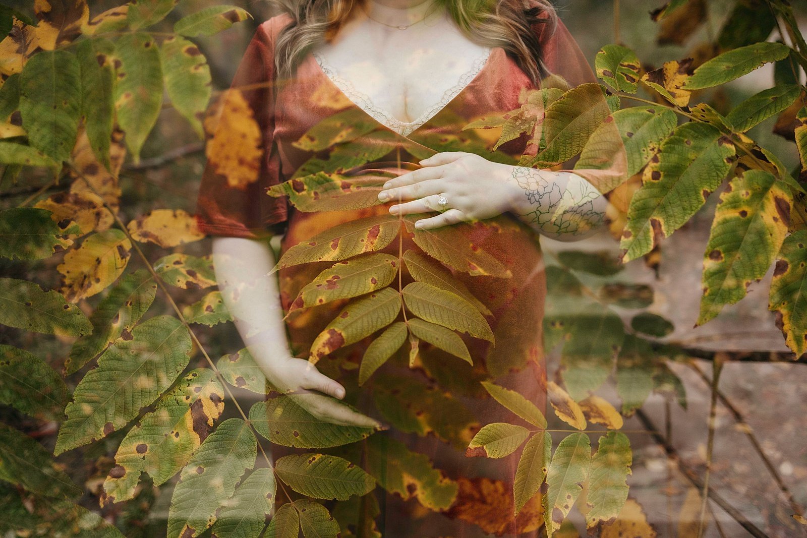  Woman with foliage all around holding her growing belly in a red dress.  