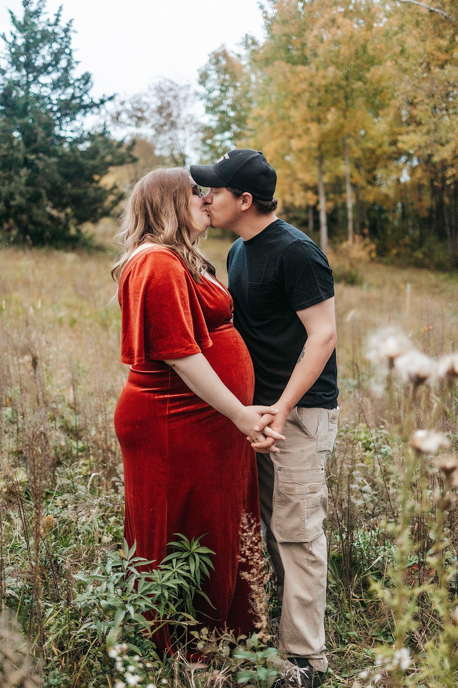  Husband kissing his pregnant wife in a field for their maternity photo shoot.  