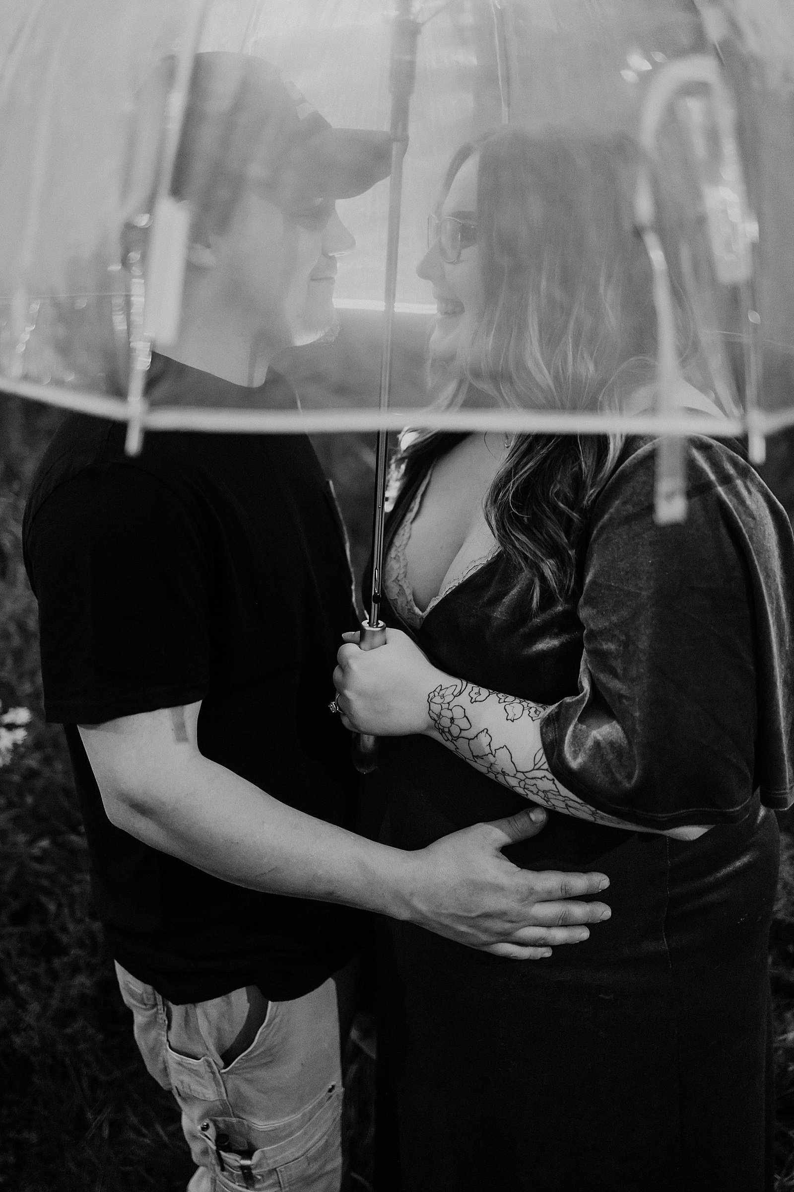  Married couple snuggling under a clear umbrella for their photo shoot before their new baby arrives. 