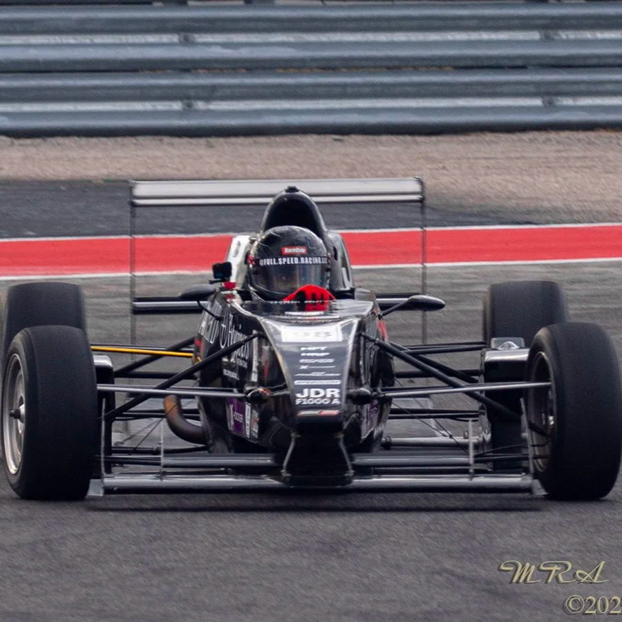 Black open-wheel race car on a race track with a driver in a helmet.