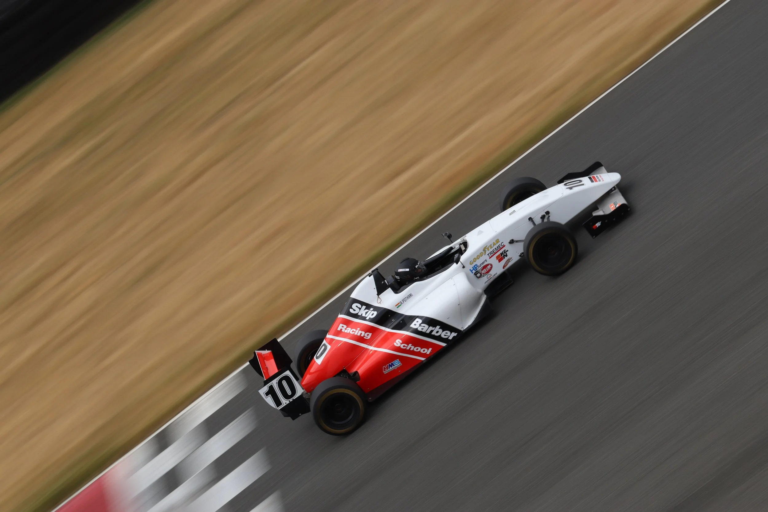 A race car with a white and red color scheme speeding on a track, with logos and sponsor decals, capturing motion blur.
