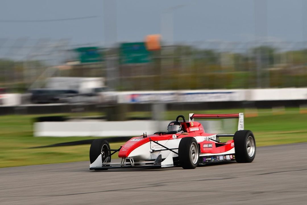 Red and white open-wheel race car on a racetrack with blurred background.